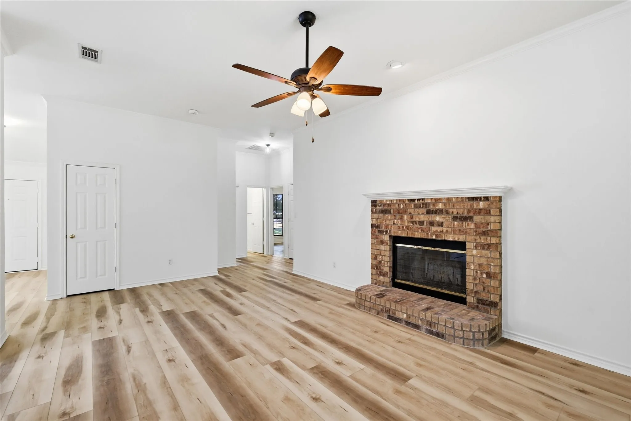 Spacious living area featuring wood-finish flooring, a brick fireplace with a mantle, and a ceiling fan with integrated lighting