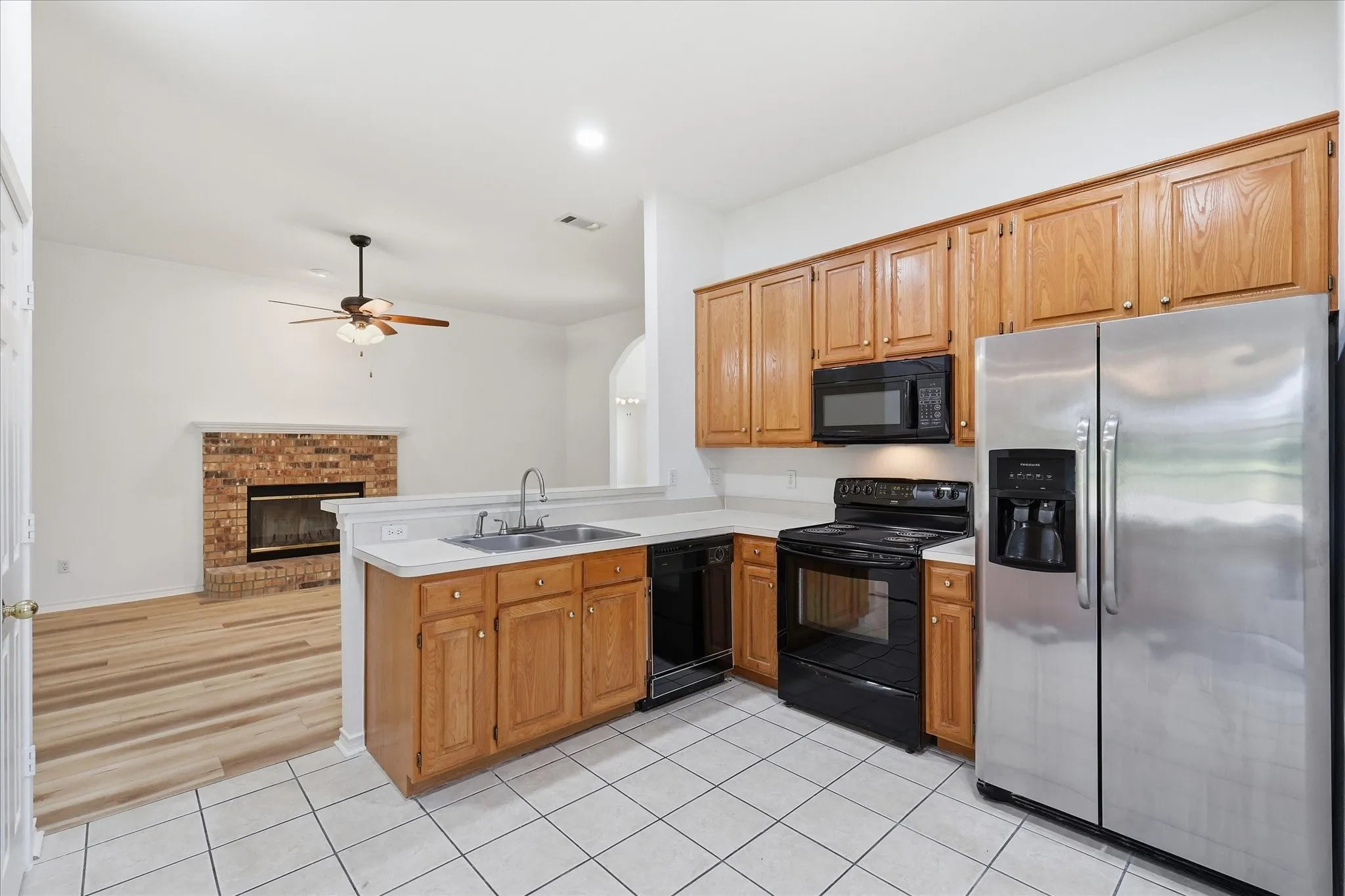 Kitchen featuring wood cabinetry, white tile flooring, stainless steel refrigerator, and black appliances
