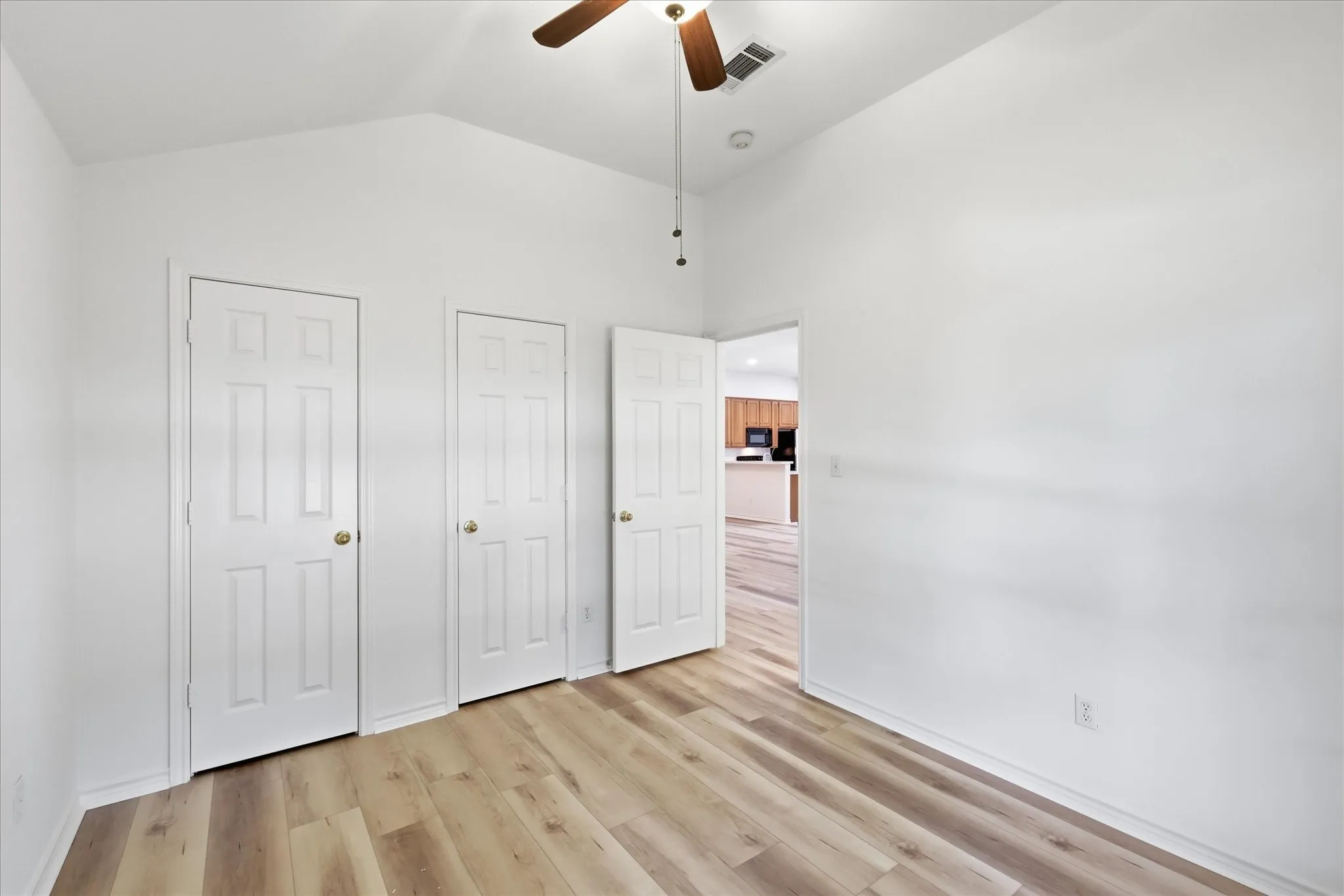 Vaulted ceiling with a ceiling fan, wood-finish flooring, and white paneled doors