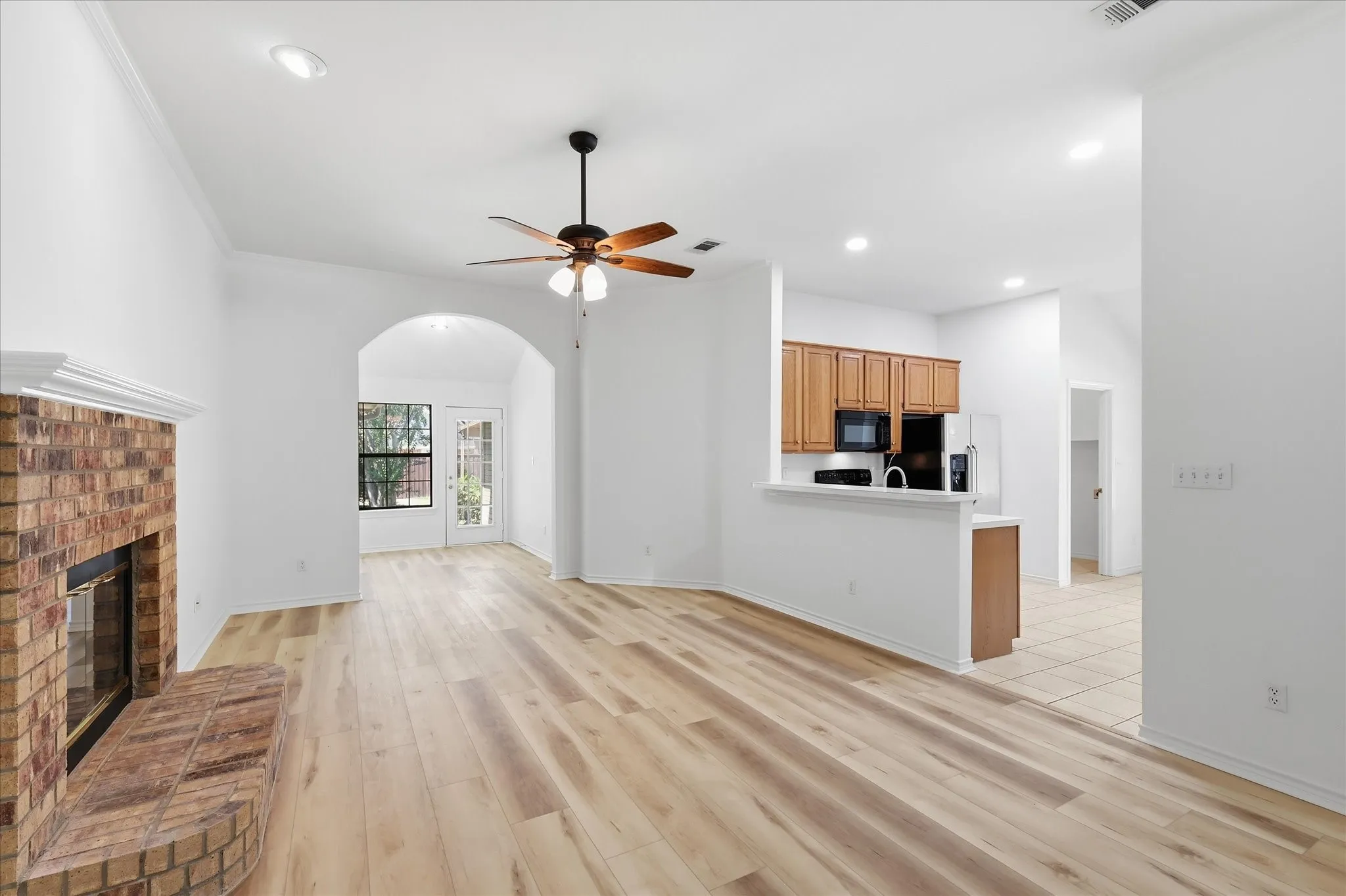 Wood-finish flooring throughout, brick fireplace with mantel, recessed lighting, and a ceiling fan