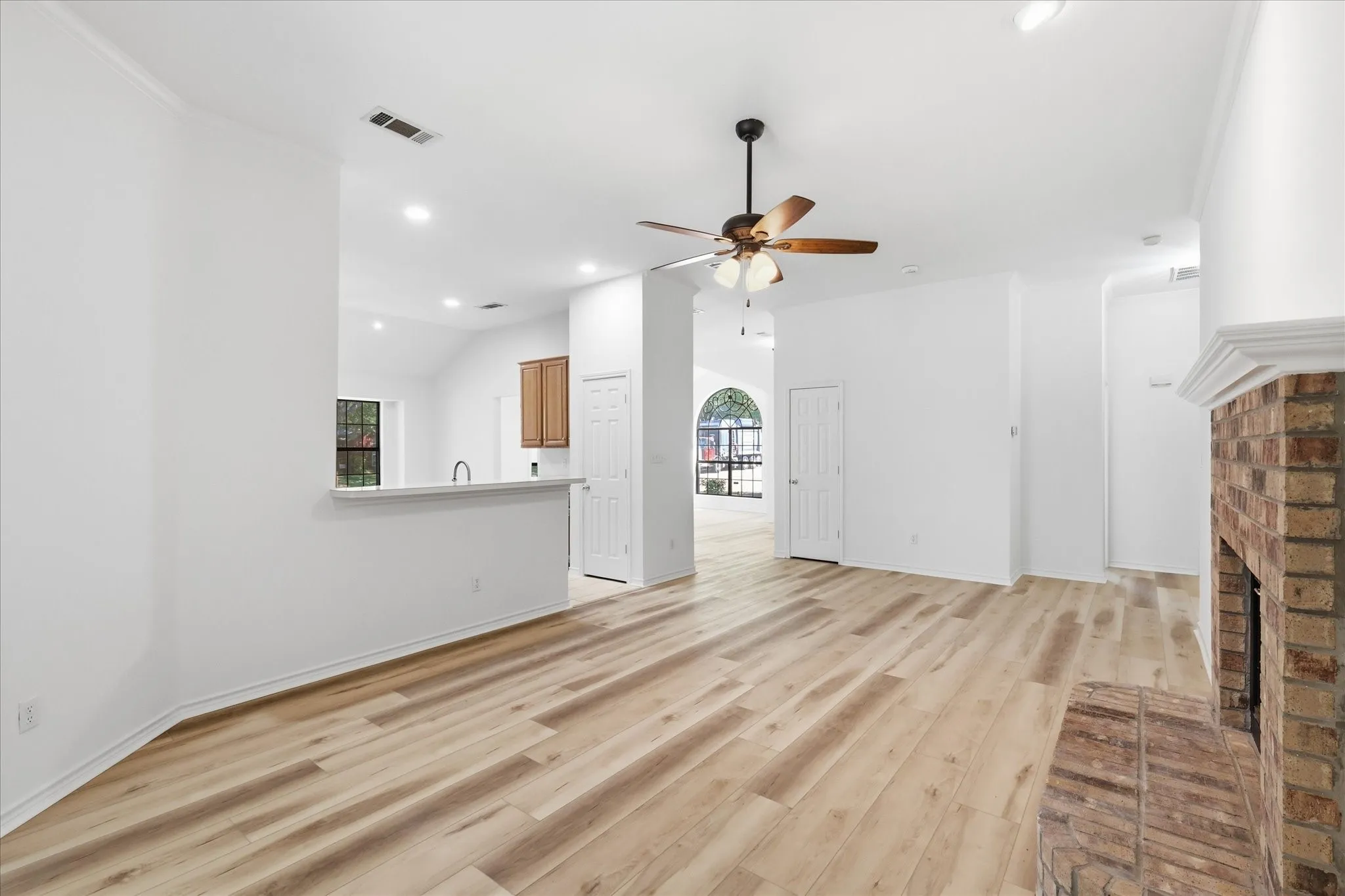 Spacious interior featuring wood-finish flooring, a brick fireplace with a white mantel, and a ceiling fan with integrated lighting