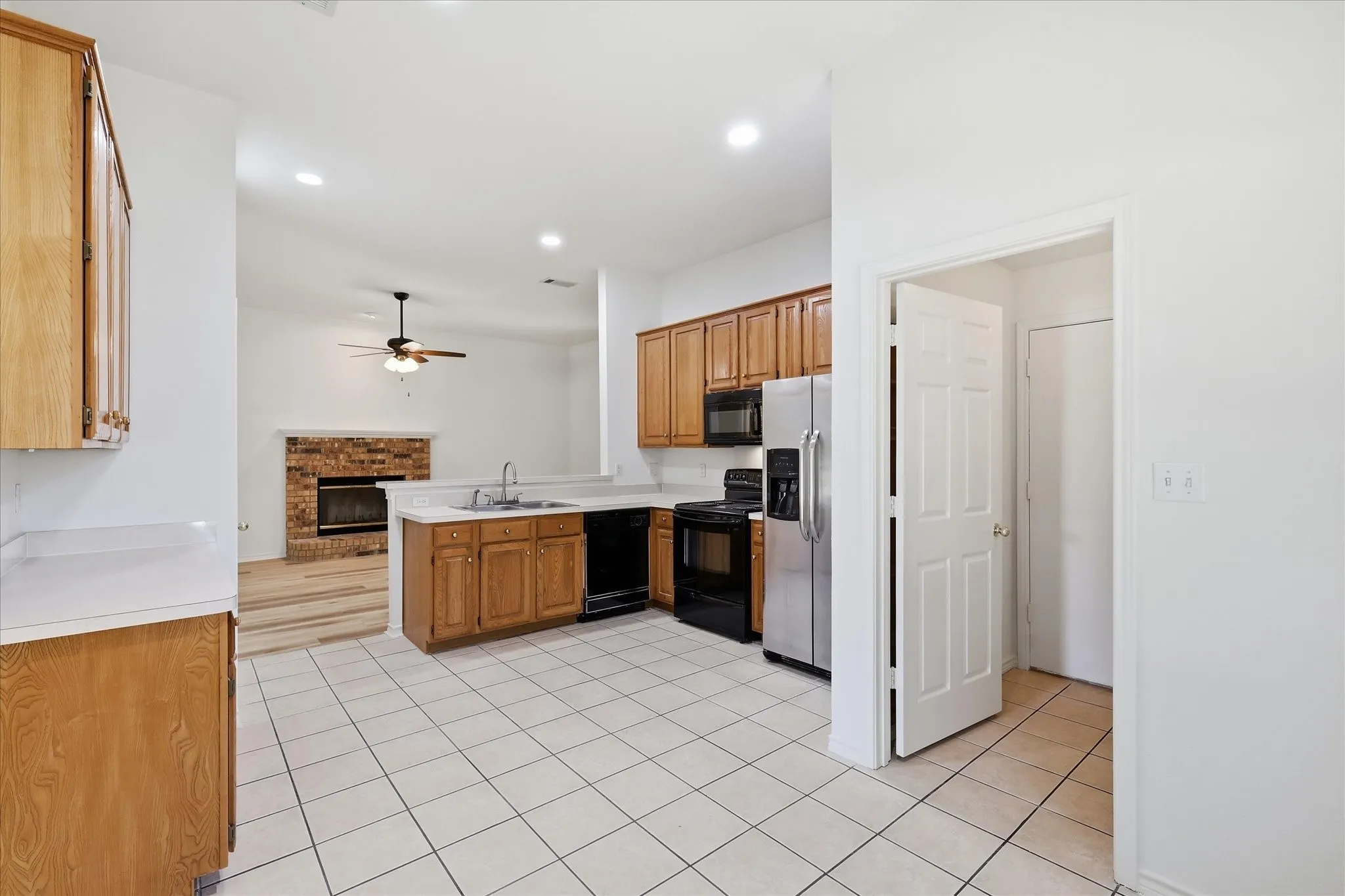 Kitchen featuring L-shaped wood cabinetry, white tile flooring, stainless steel refrigerator, and integrated black appliances