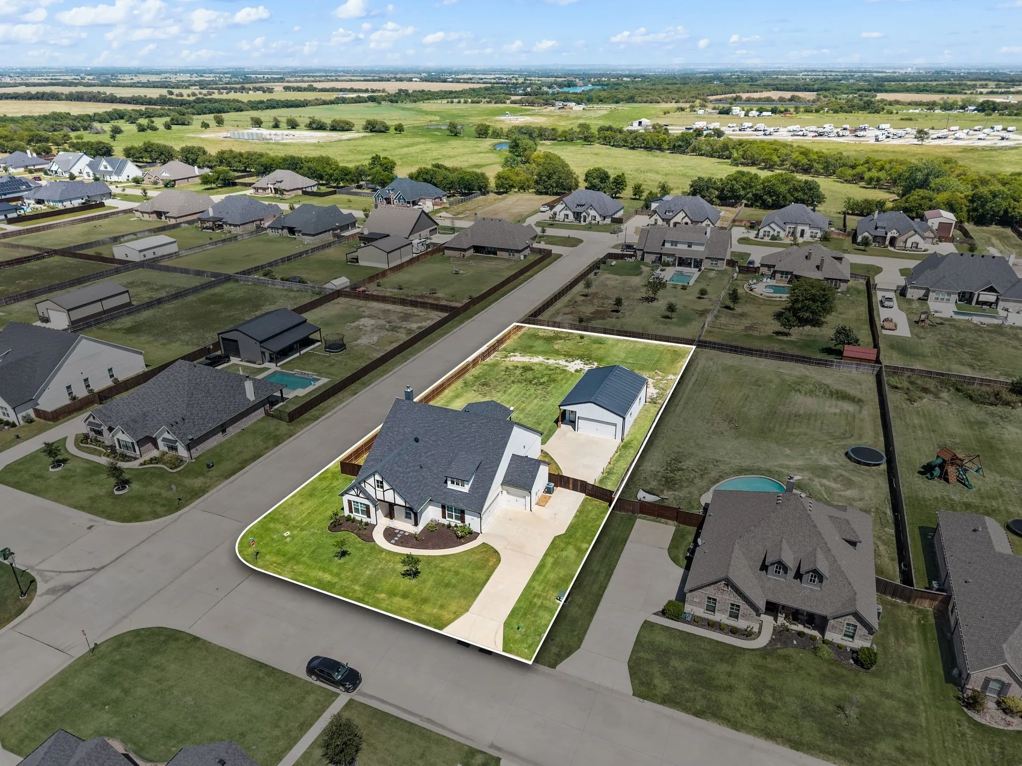 Aerial view highlighting a single-family residence with an attached garage, a detached auxiliary building, and a paved driveway, all set within a landscaped lot