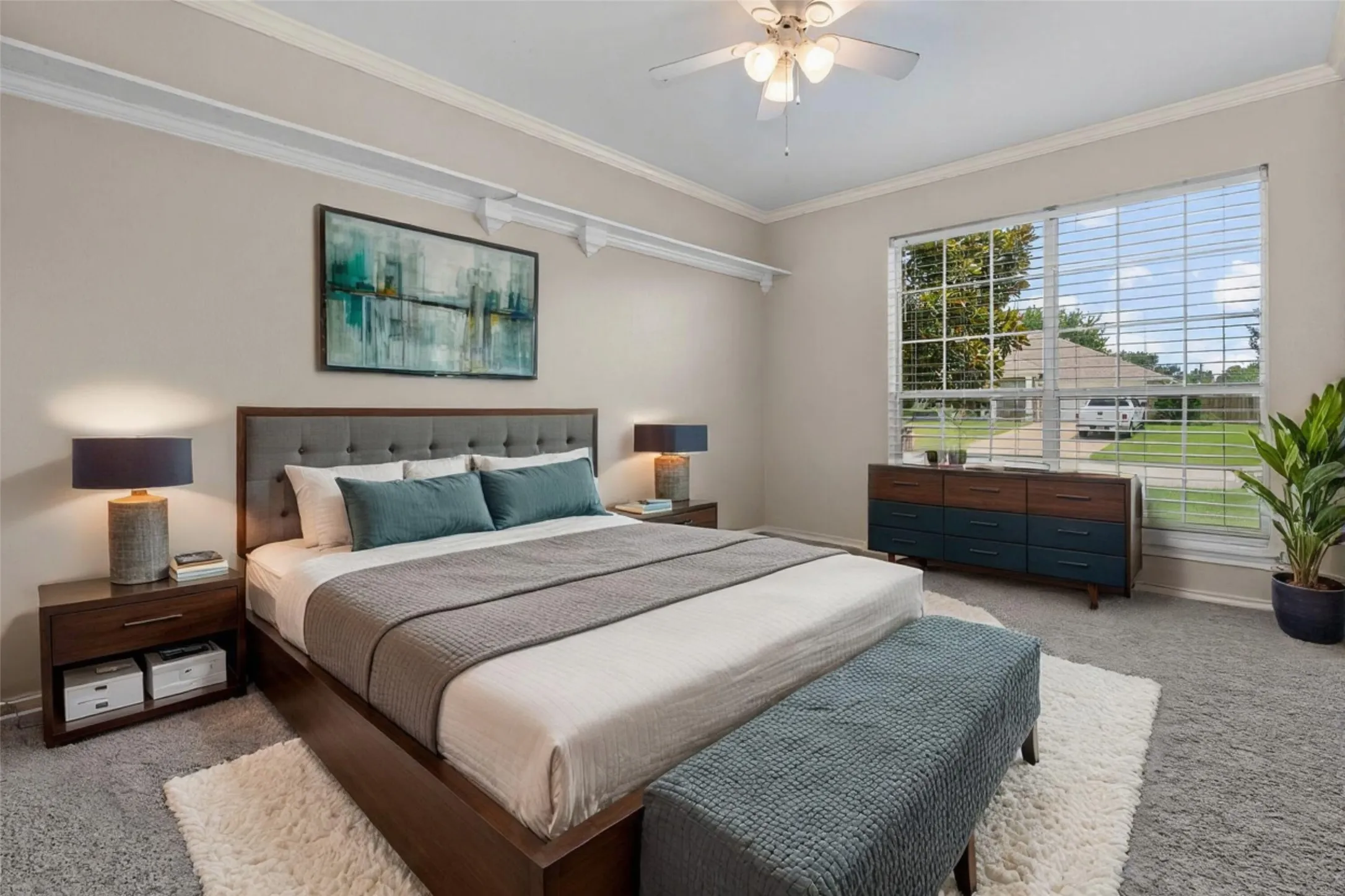 Master bedroom showcasing a wood-finish platform bed frame, dual nightstands with integrated storage, layered bedding in neutral tones, recessed ceiling with ceiling fan, and expansive sliding glass doors with plantation shutters opening to outdoor views