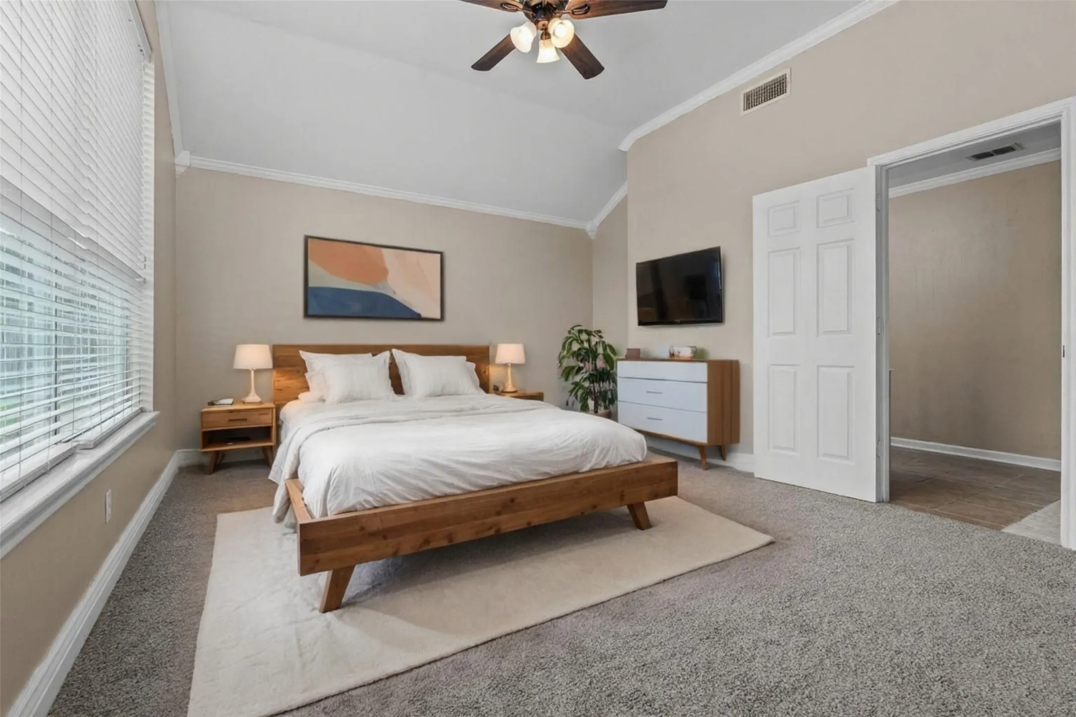 Spacious primary bedroom featuring a wood-frame bed, neutral wall finishes, carpet flooring, and a large area rug