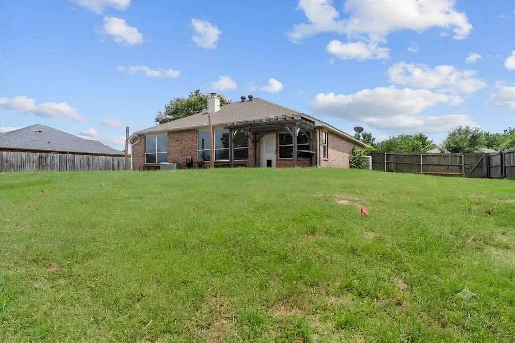 Expansive backyard featuring a manicured lawn, full perimeter wood fencing, and a brick exterior with a covered patio