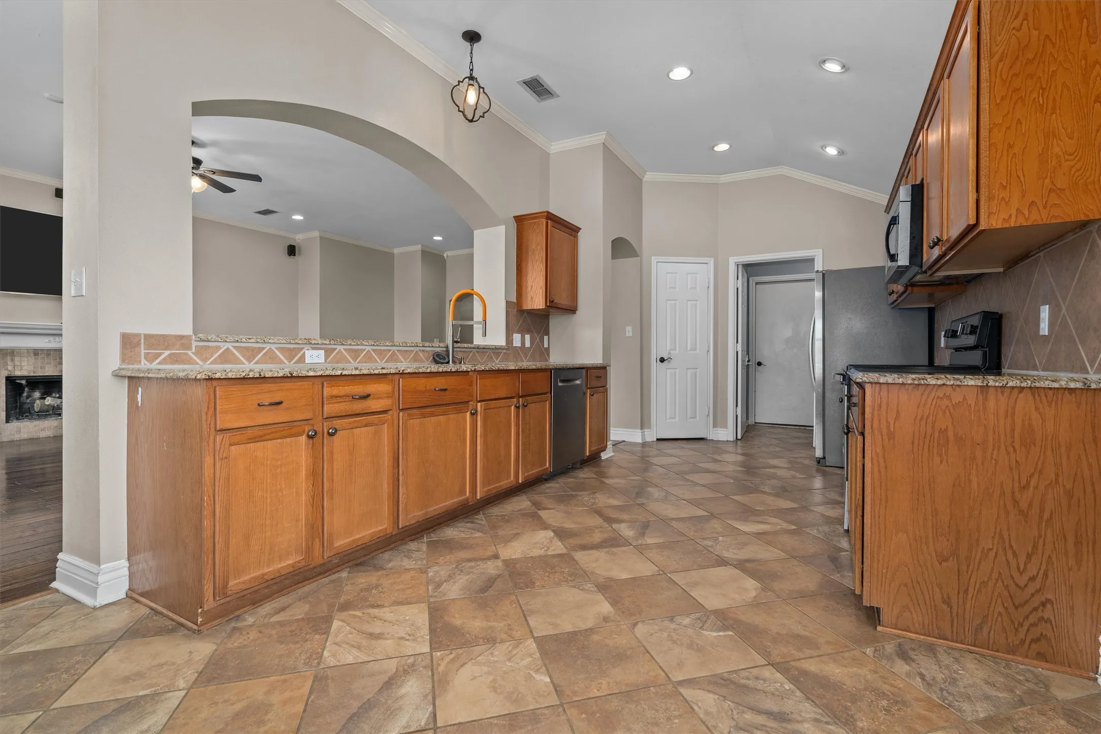 Spacious kitchen and dining area showcasing rich wood cabinetry, dual sink vanity with decorative backsplash, stainless steel appliances, recessed ceiling lighting, and diagonal tile flooring throughout the open layout