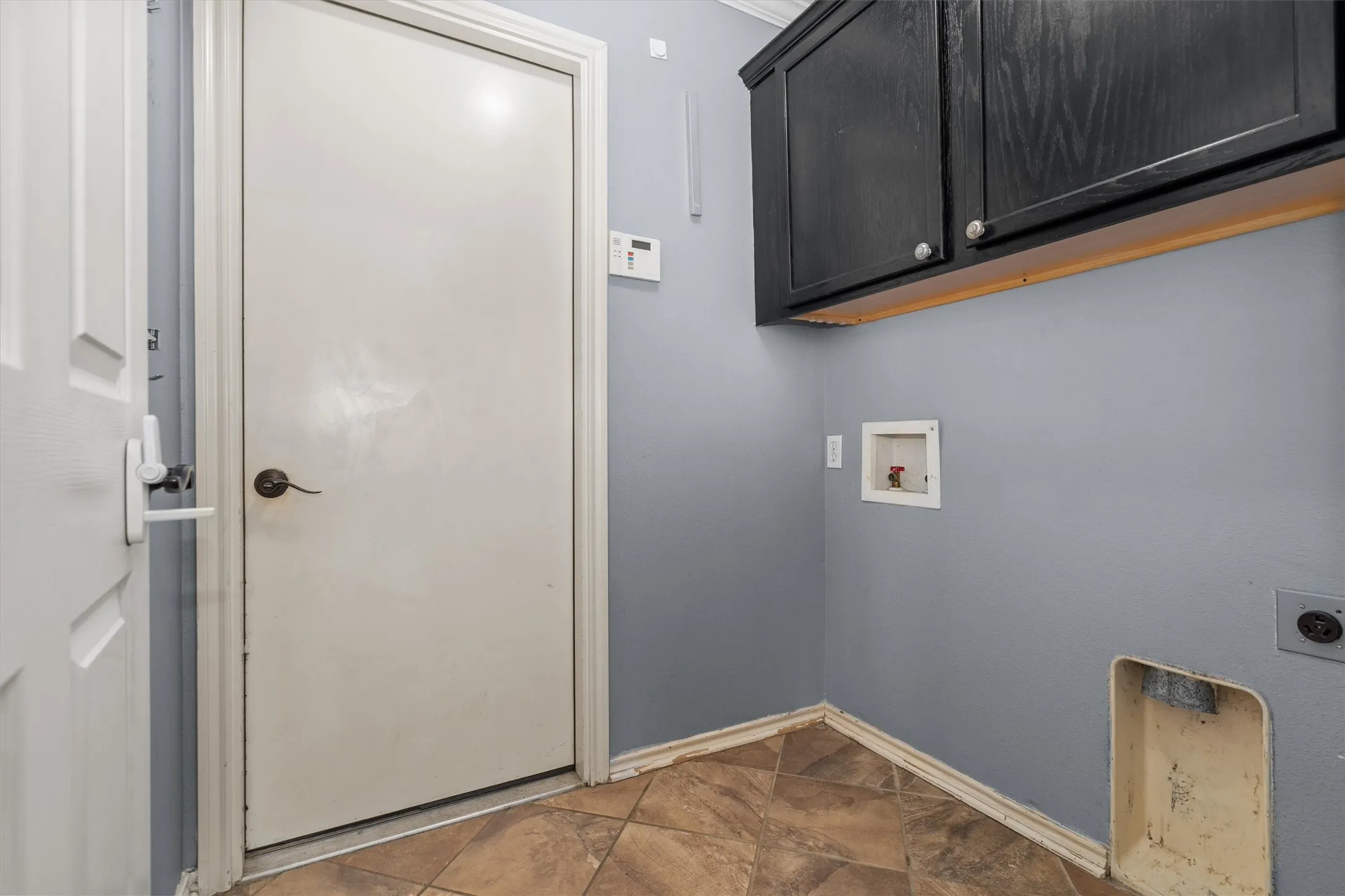Utility room featuring blue-gray painted walls, dark cabinetry with wood-finish trim, wood-finish flooring, and direct entry door with hardware