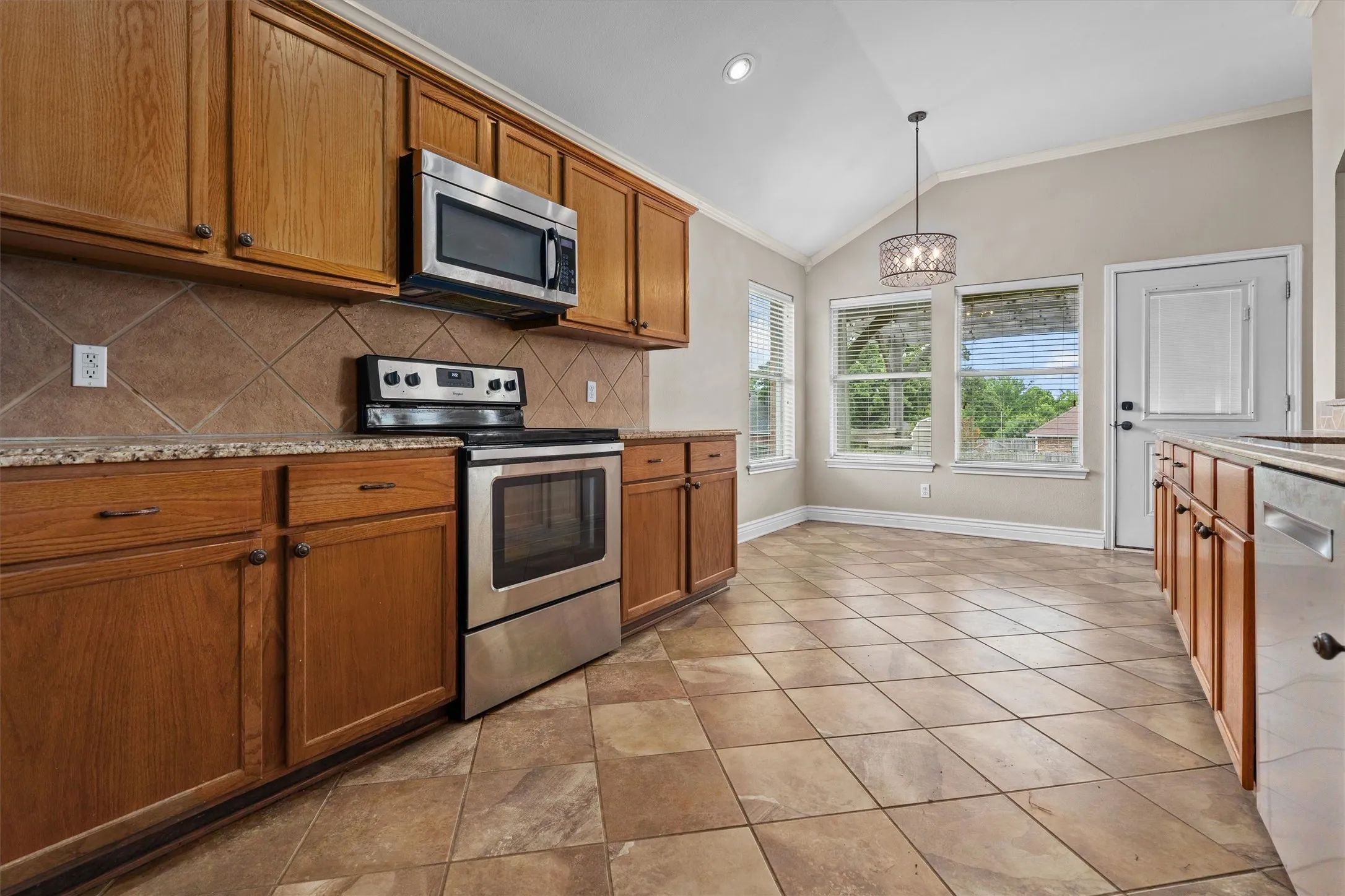 Galley-style kitchen featuring stainless steel appliances, wood cabinetry with bronze hardware, granite countertops, and diagonal tile flooring