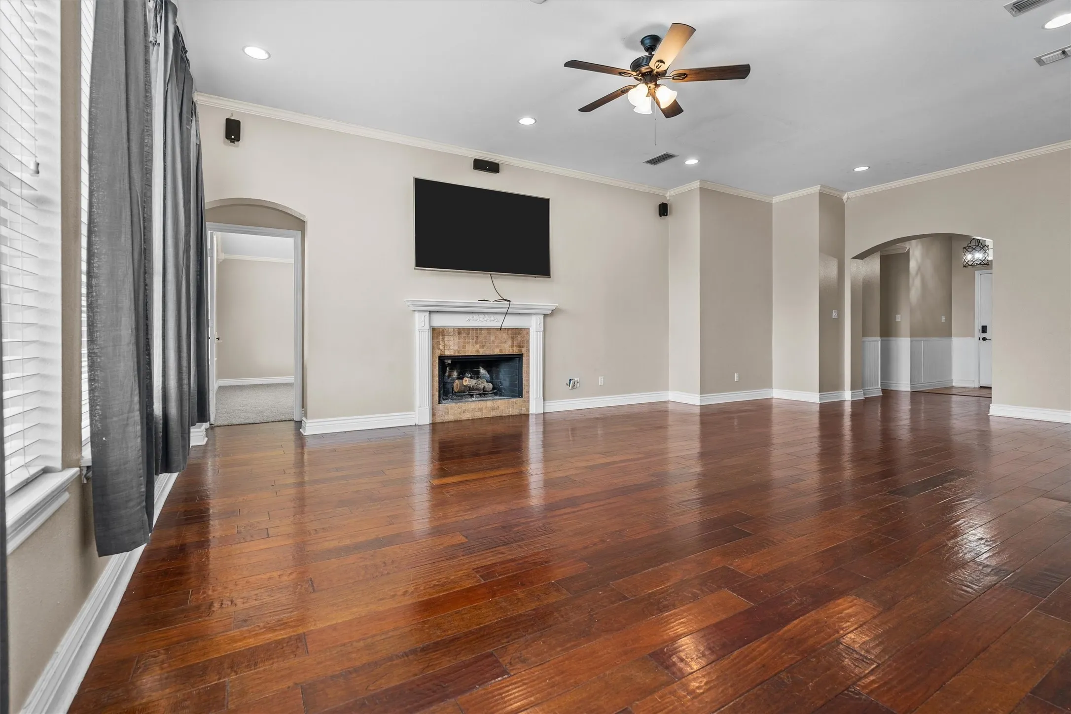 Spacious living area showcasing gleaming hardwood flooring, a ceiling fan with brushed metal finish, and recessed lighting throughout