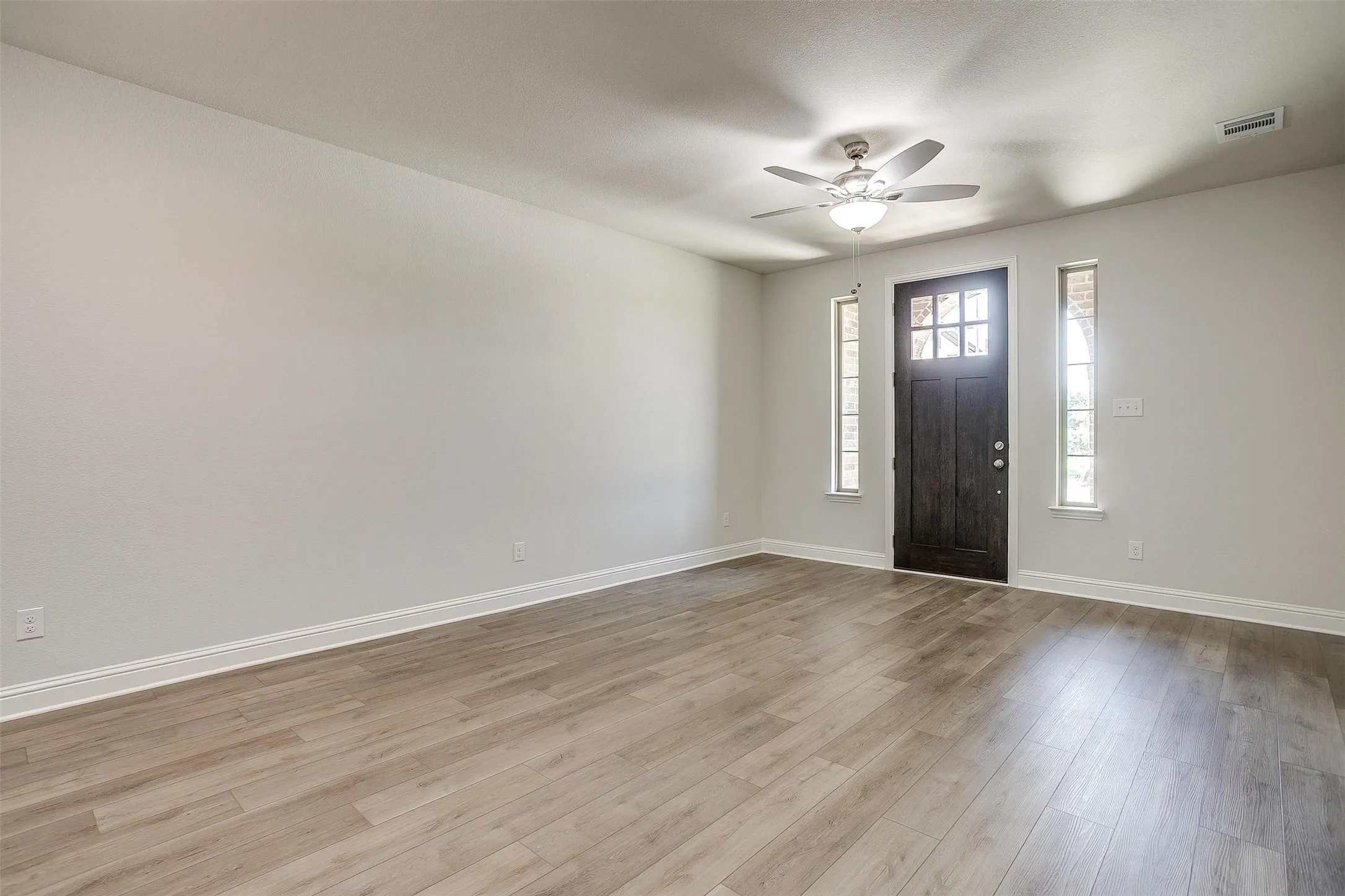 Wood-finish flooring, dark wood-paneled door with glass inserts, two sidelight windows, and a ceiling fan with integrated lighting