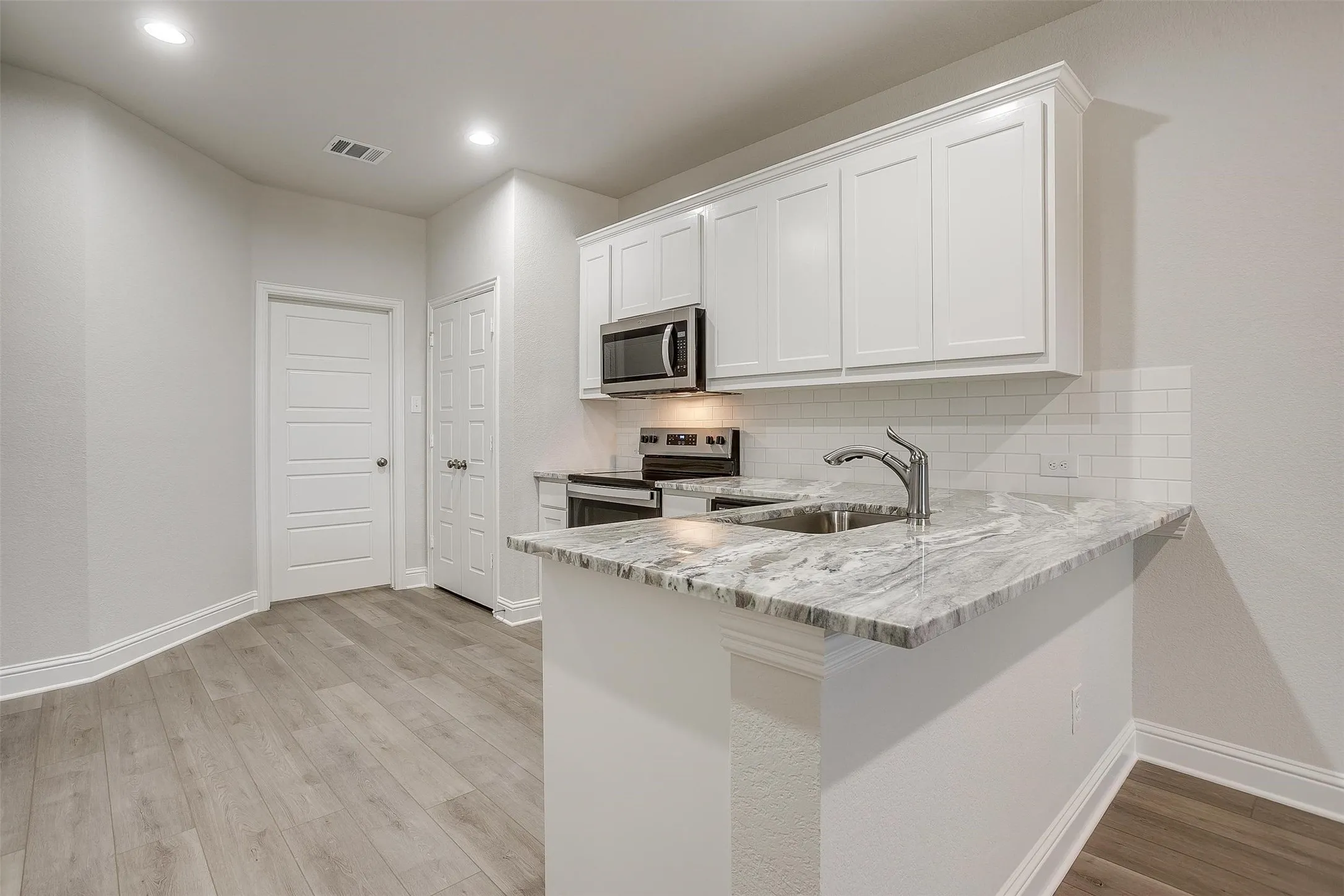 Kitchen featuring white cabinetry, stainless steel appliances, a subway tile backsplash, a sink with a gooseneck faucet, and light wood-finish flooring