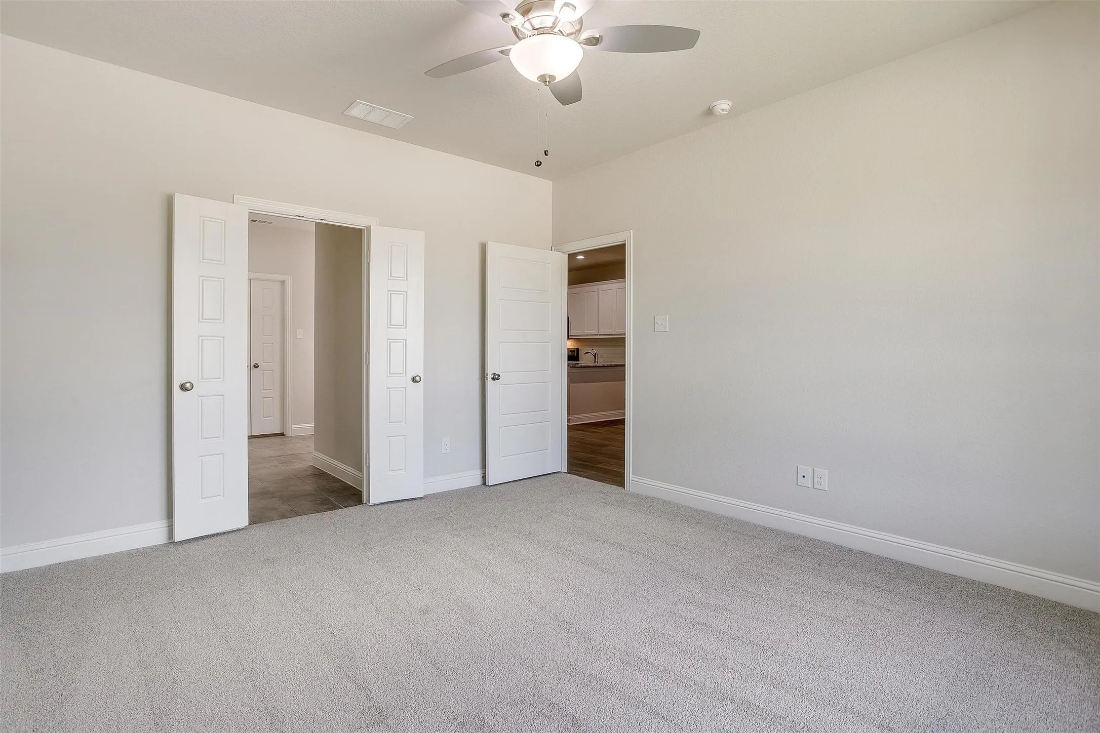 Spacious primary bedroom with neutral carpeting, ceiling fan with integrated lighting, and multiple closet options including dual walk-in closets