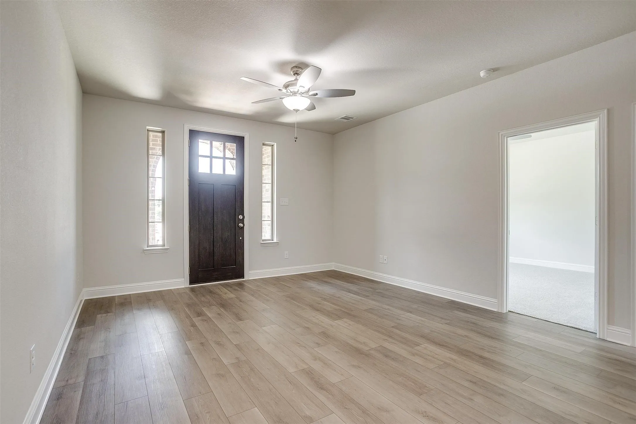 Wood-finish flooring throughout, ceiling fan, and paneled entry door with sidelights