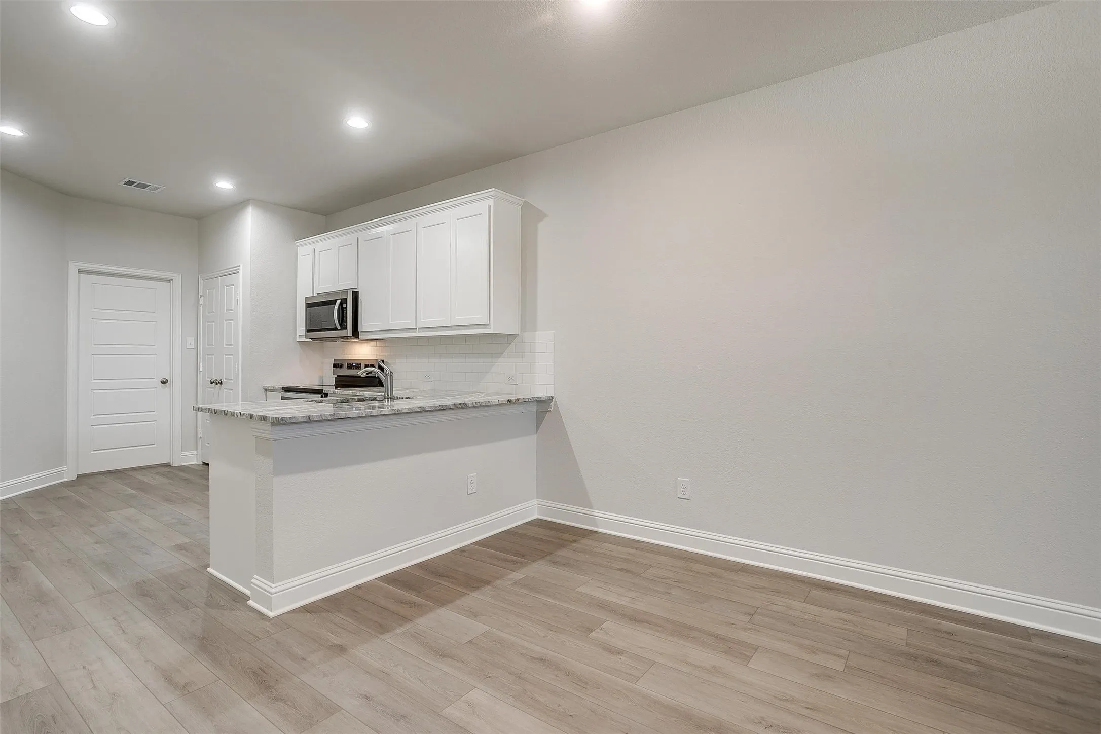 Kitchenette with white cabinetry, stainless steel microwave, stone countertop, tile backsplash, and recessed lighting