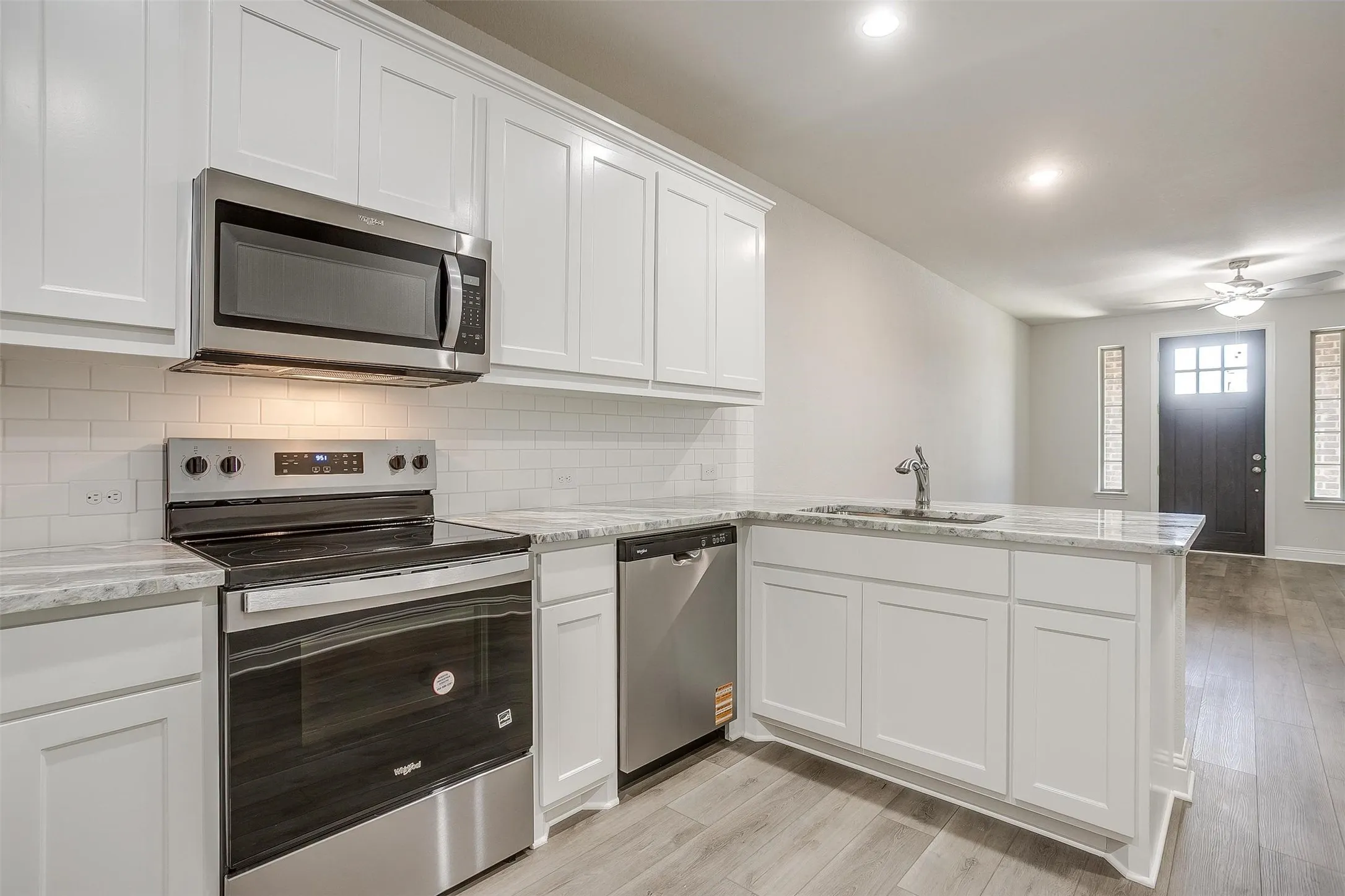 White shaker-style cabinetry, stainless steel appliances, light-toned countertops, subway tile backsplash, and wood-finish flooring