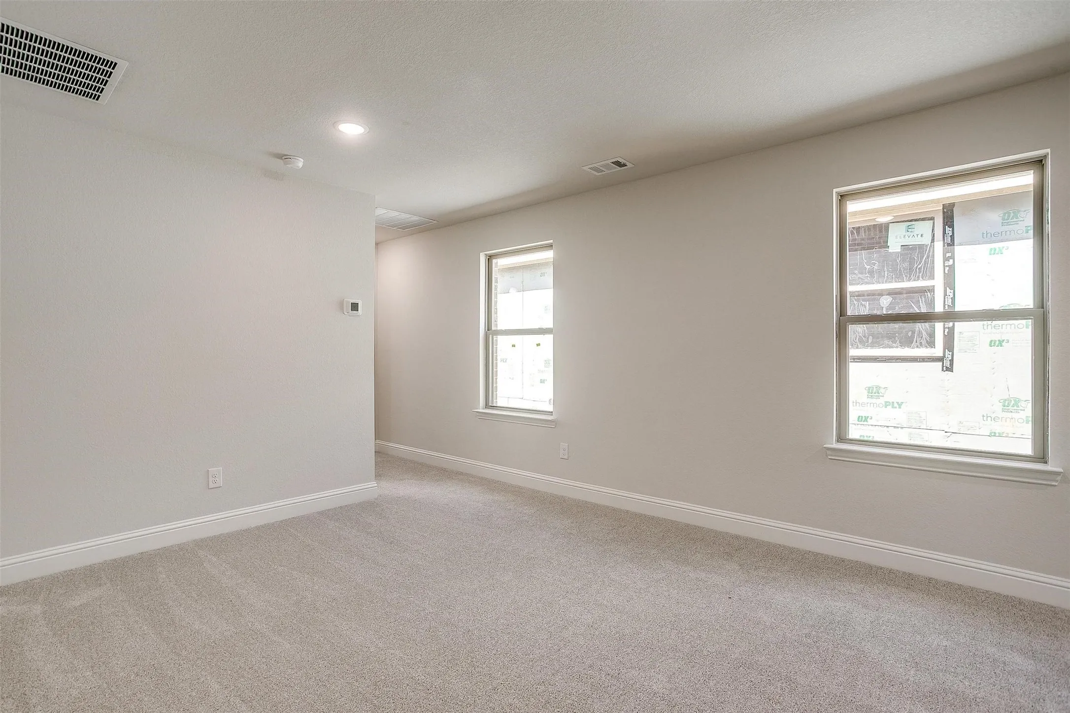 Plush carpet flooring, recessed ceiling lighting, two windows, and baseboard trim