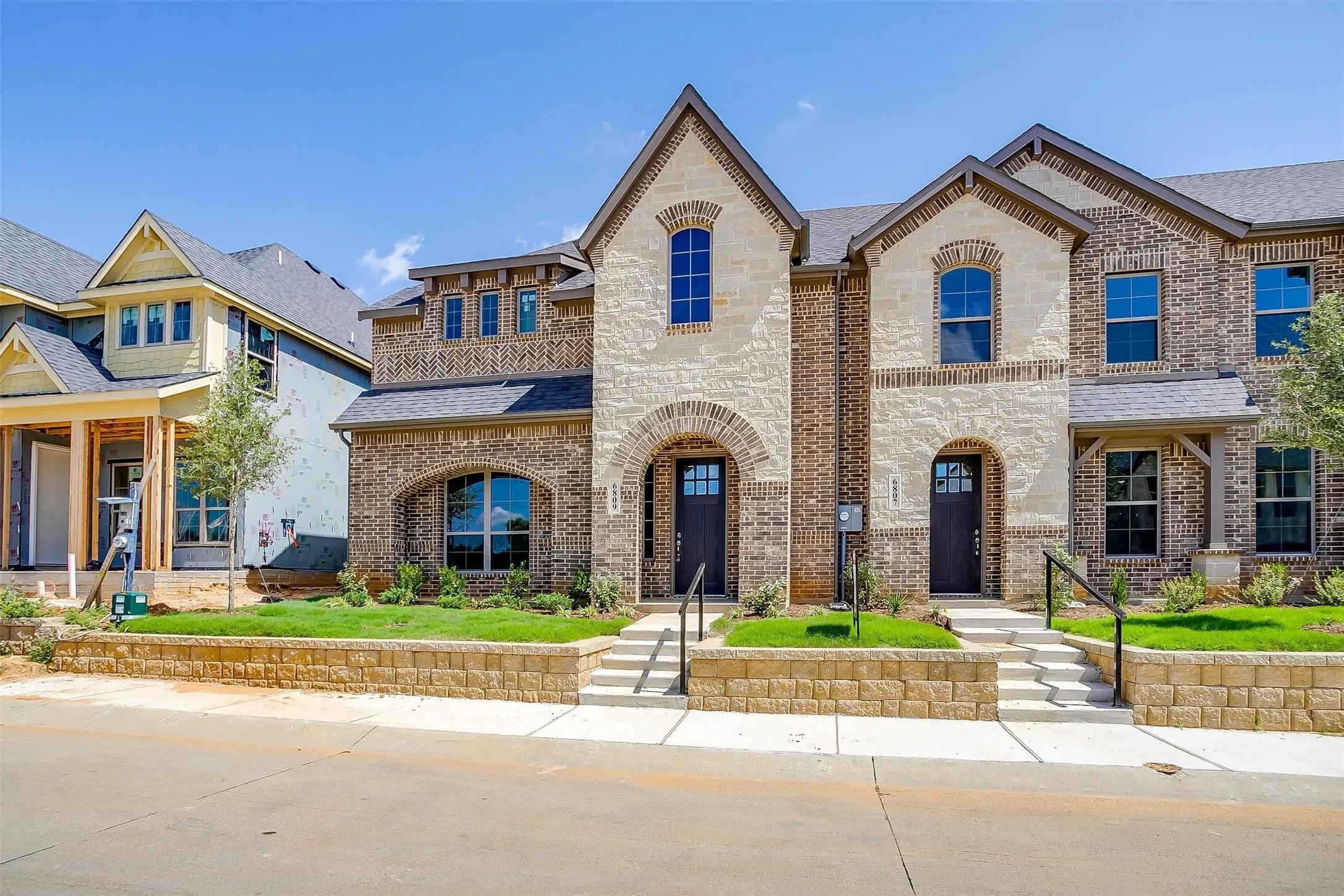 Brick and stone facade with arched entryways, dark-framed windows, a gabled roofline, and landscaped front yard