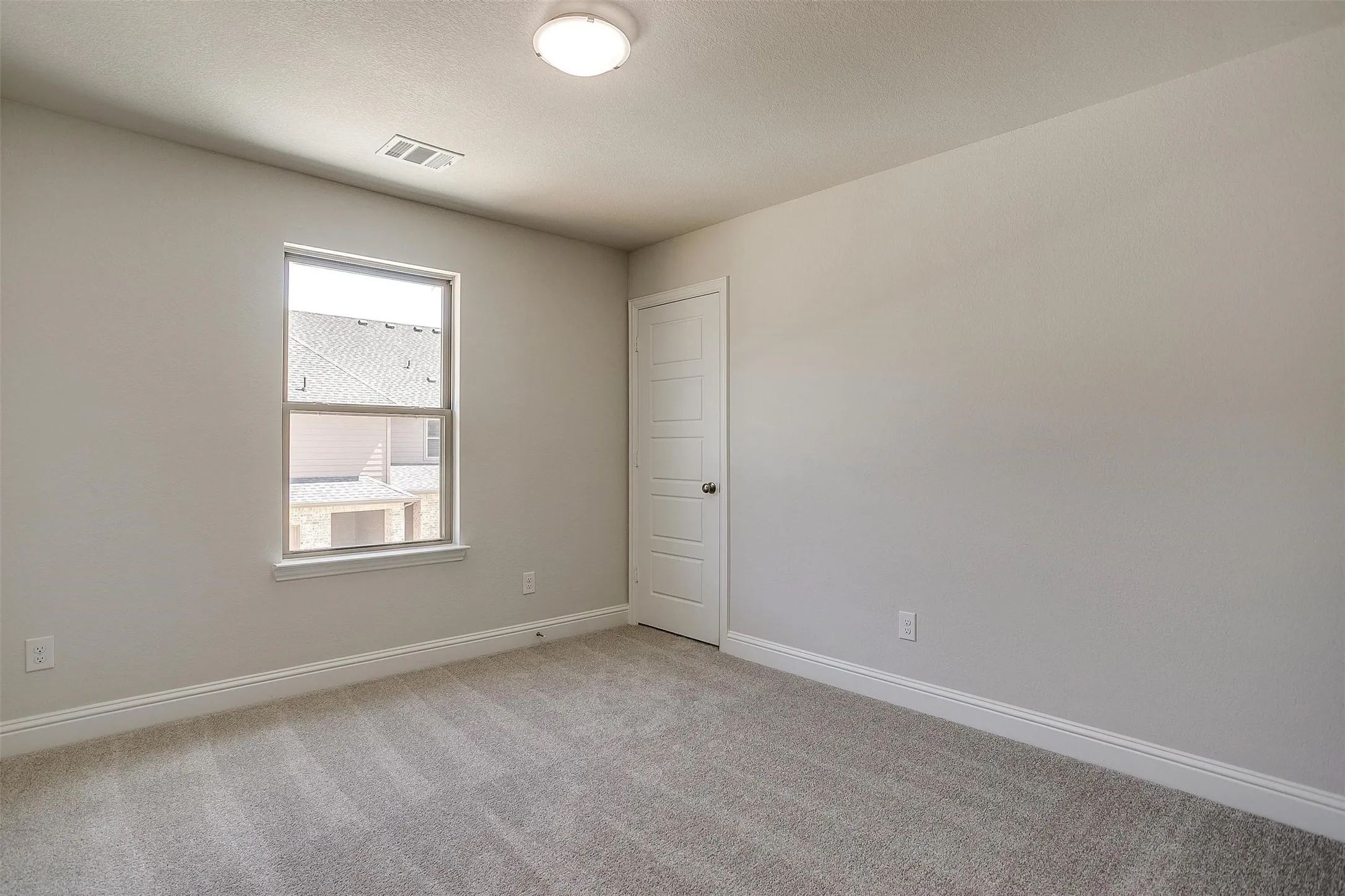 Neutral tone wall finish, textured carpet flooring, single window, flush mount ceiling light, and a paneled interior door
