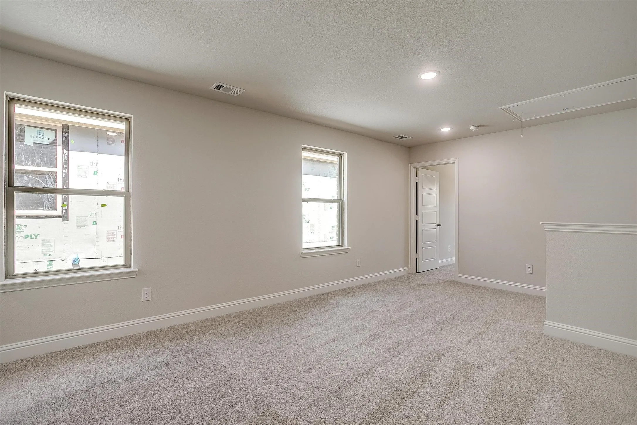 Recessed lighting, light gray carpeting, neutral wall color, two windows, and a paneled door