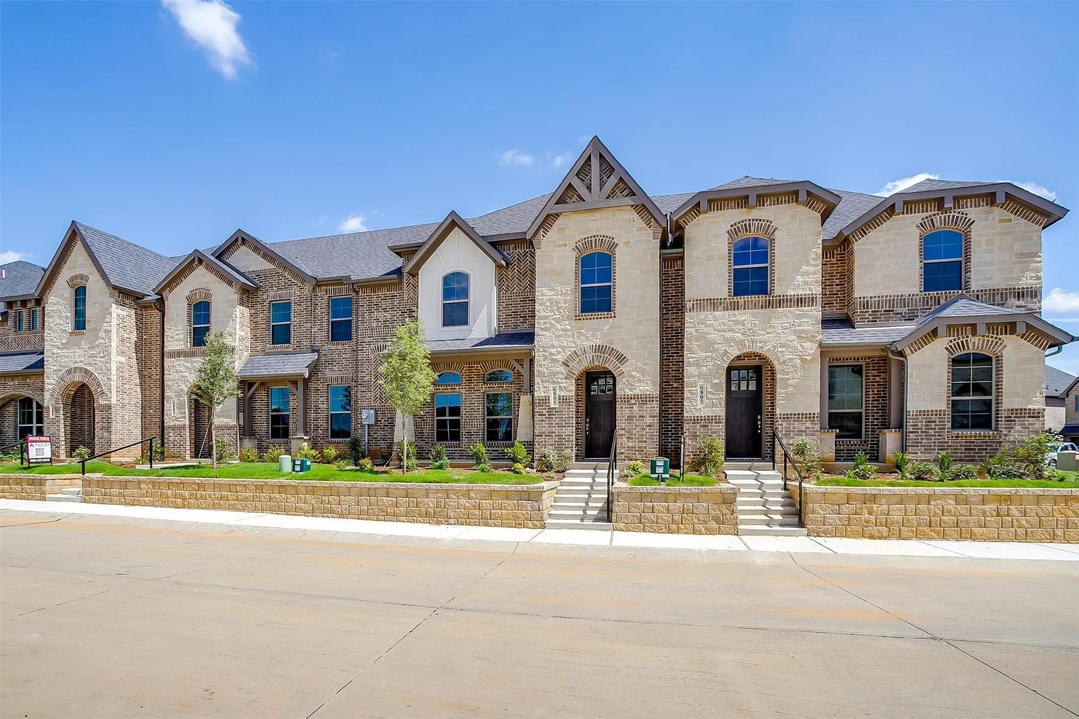 Brick and stone facade with arched windows, prominent gables, dark roof, and paved driveway