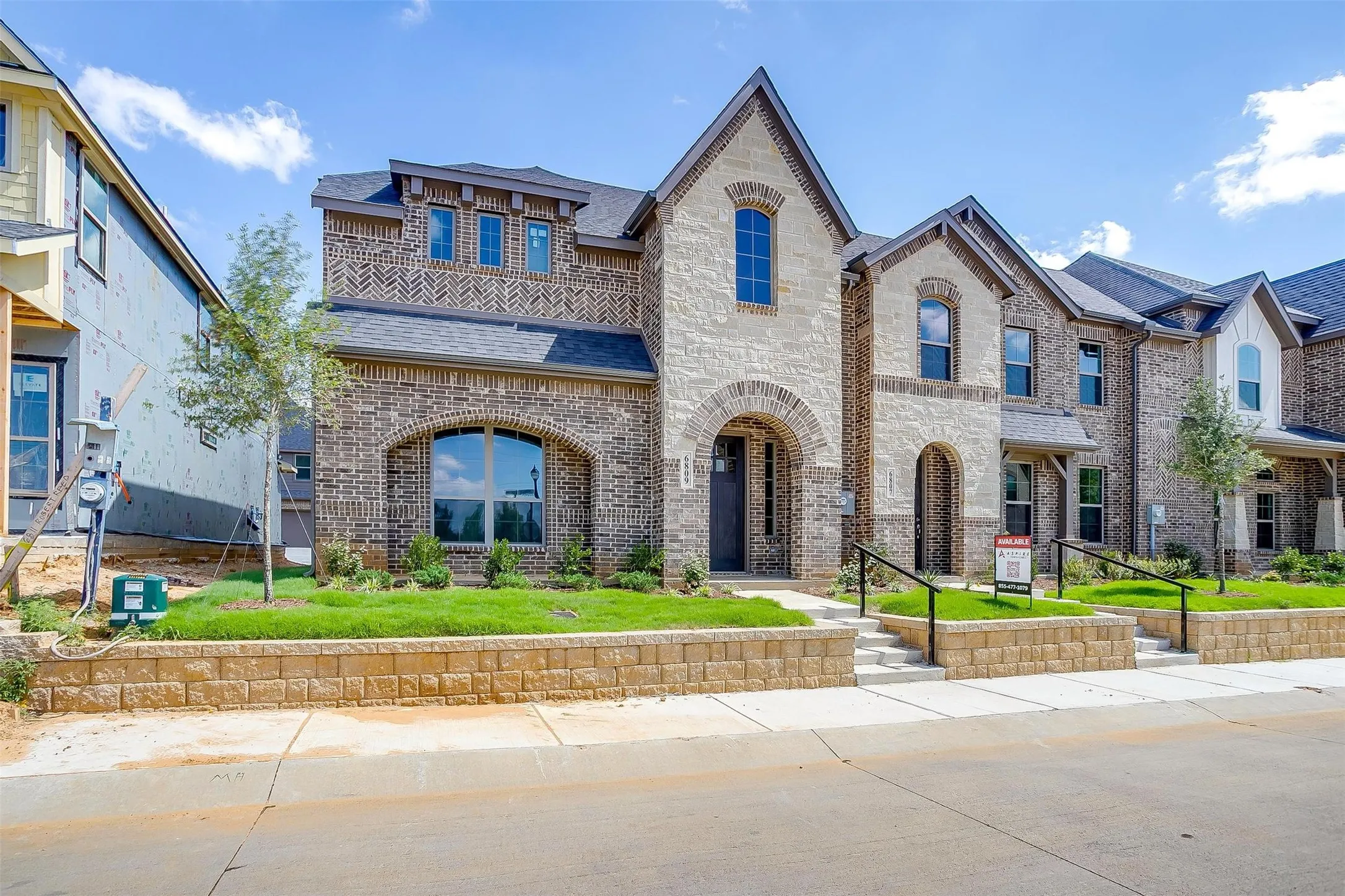 Stone and brick exterior with arched entryways, dark shingle roof, and a segmented retaining wall