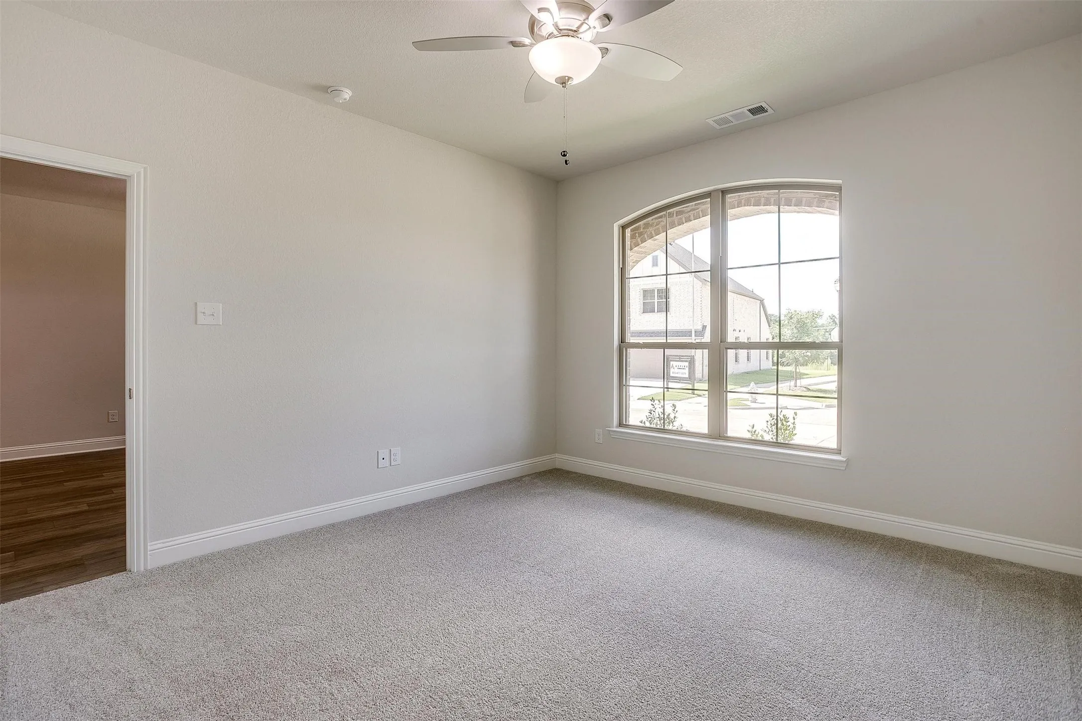 Carpeted flooring, arched window with grid, ceiling fan with integrated lighting, and a white trim package