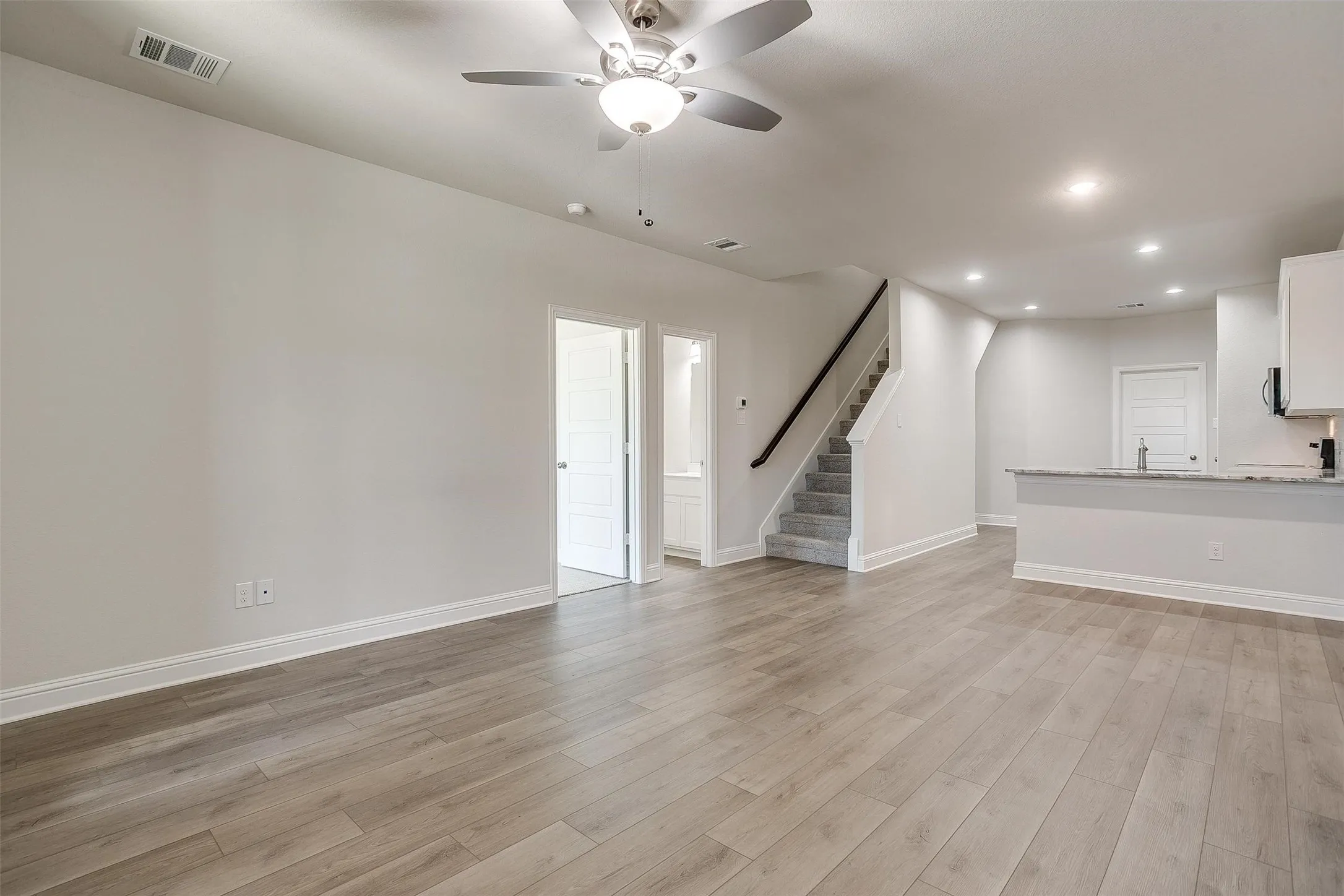 Open-concept living space featuring wood-finish flooring, recessed lighting, a ceiling fan, and staircase with carpeted treads