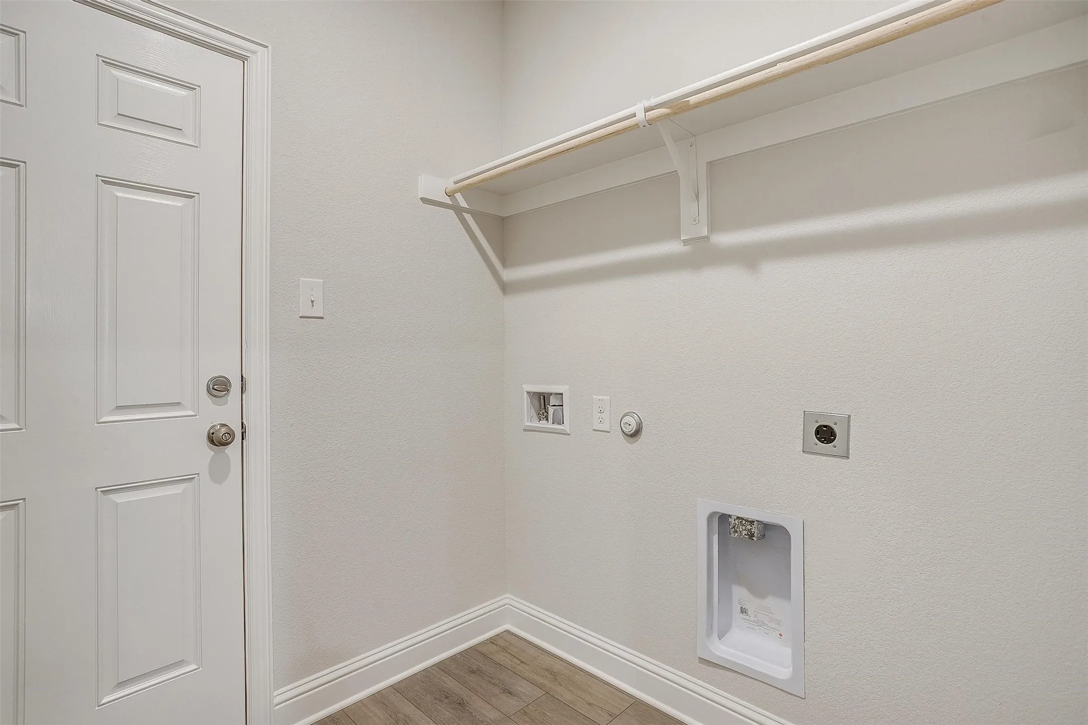 Dedicated laundry room featuring a metal shelving unit, wood-finish flooring, and convenient washer/dryer hookups