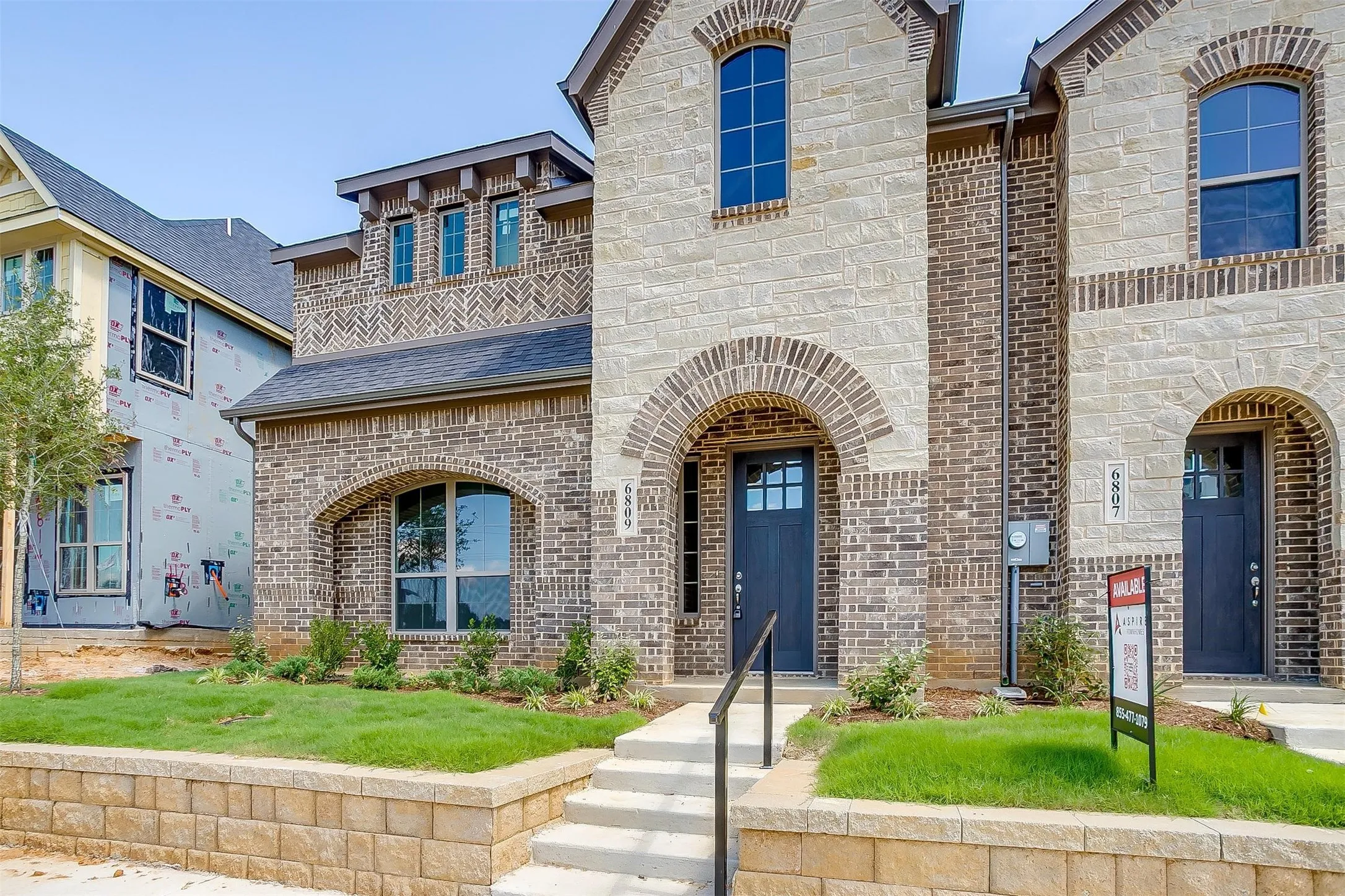 Stone and brick exterior with arched entryways, dark paneled doors, and a retaining wall