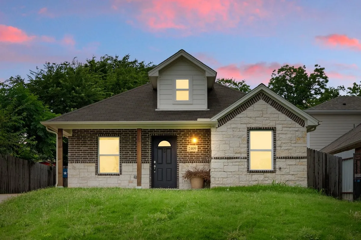 Brick and stone facade with dark shingles, featuring a dormer and covered front entry