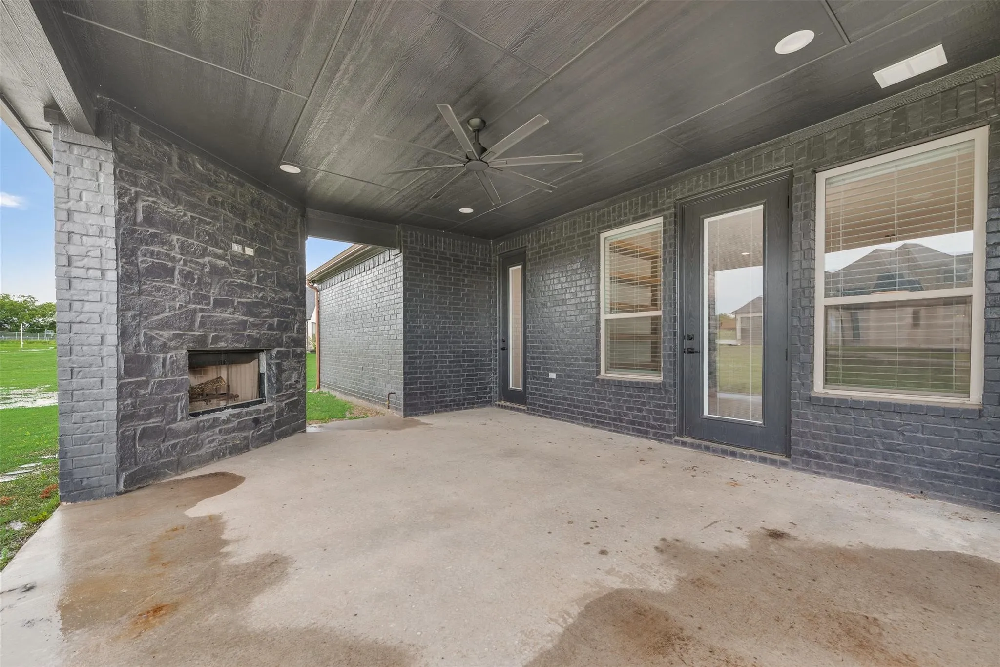 Covered patio featuring an outdoor fireplace with stone surround, a ceiling fan, recessed lighting, and brick exterior walls