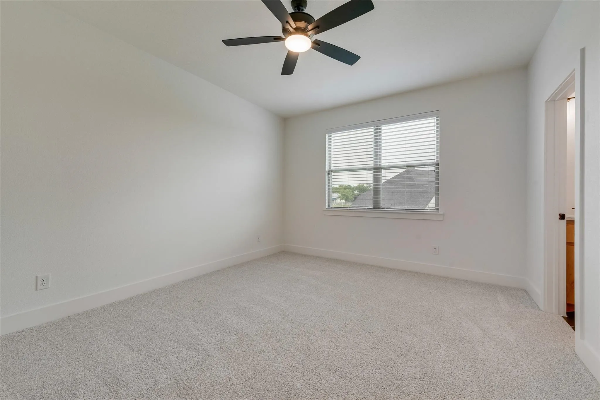 Spacious room featuring light-colored carpeting, a ceiling fan with integrated lighting, a window with blinds, and white baseboards