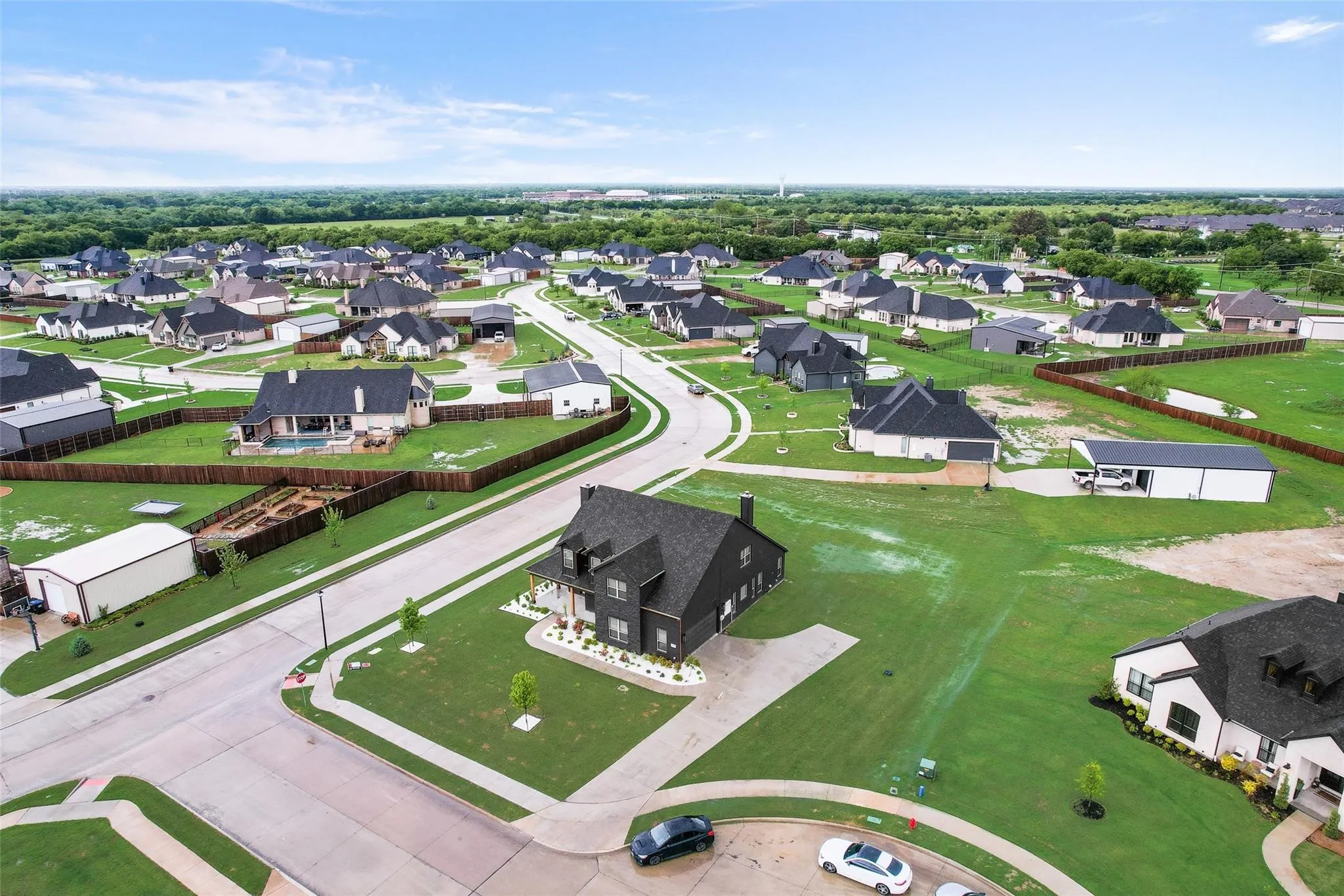Modern residential neighborhood featuring single-family homes with dark roofs and light exteriors, expansive green lawns, and curving streets
