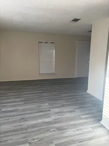 Spacious room with gray wood-finish flooring, neutral wall tones, and a window with white blinds