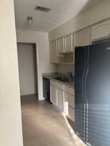Kitchen featuring white paneled cabinetry, light-toned tiled flooring, a double basin sink, and an integrated black refrigerator
