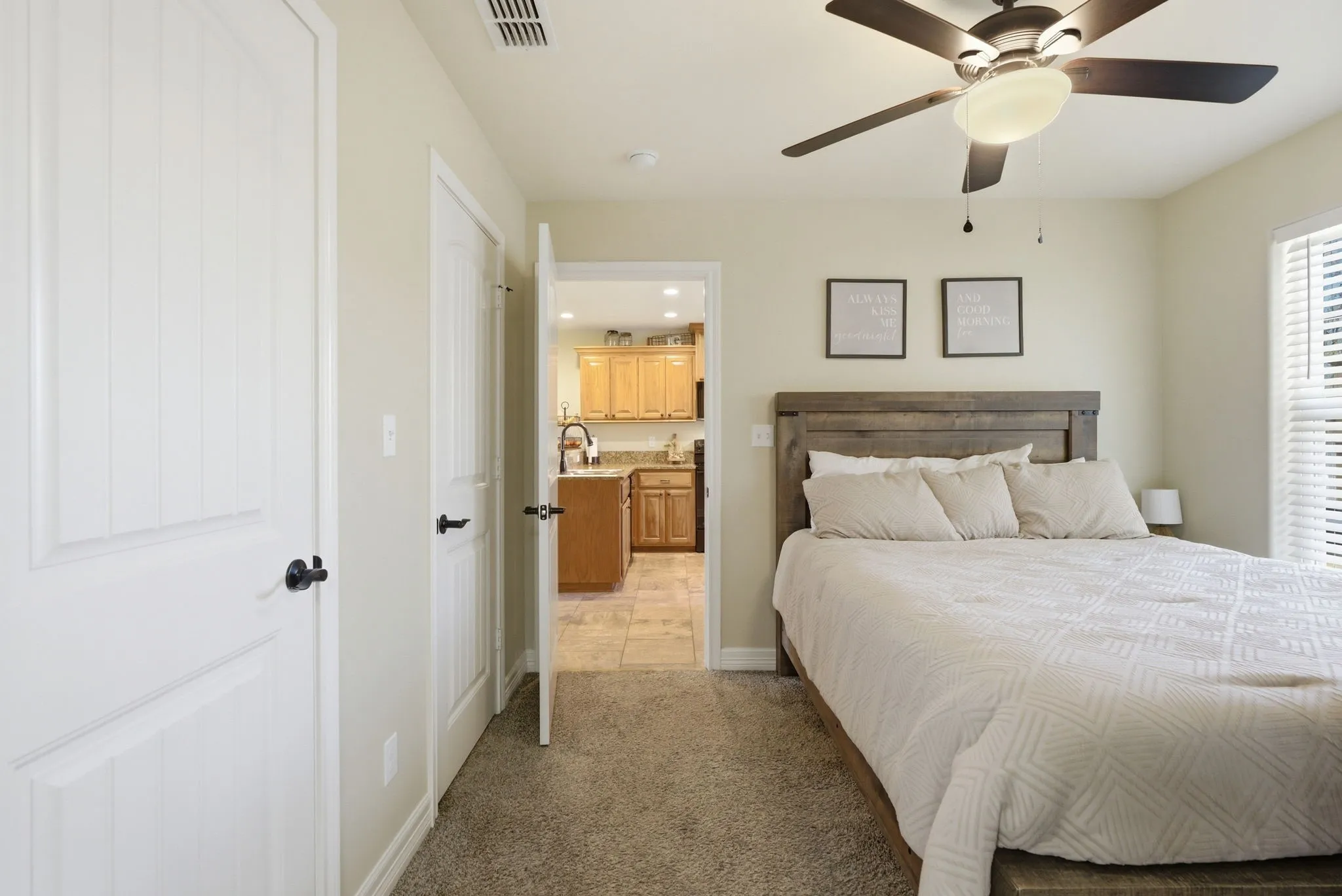 Ceiling fan with integrated lighting, wood-finish headboard, window with horizontal blinds, neutral wall paint, and plush carpet flooring