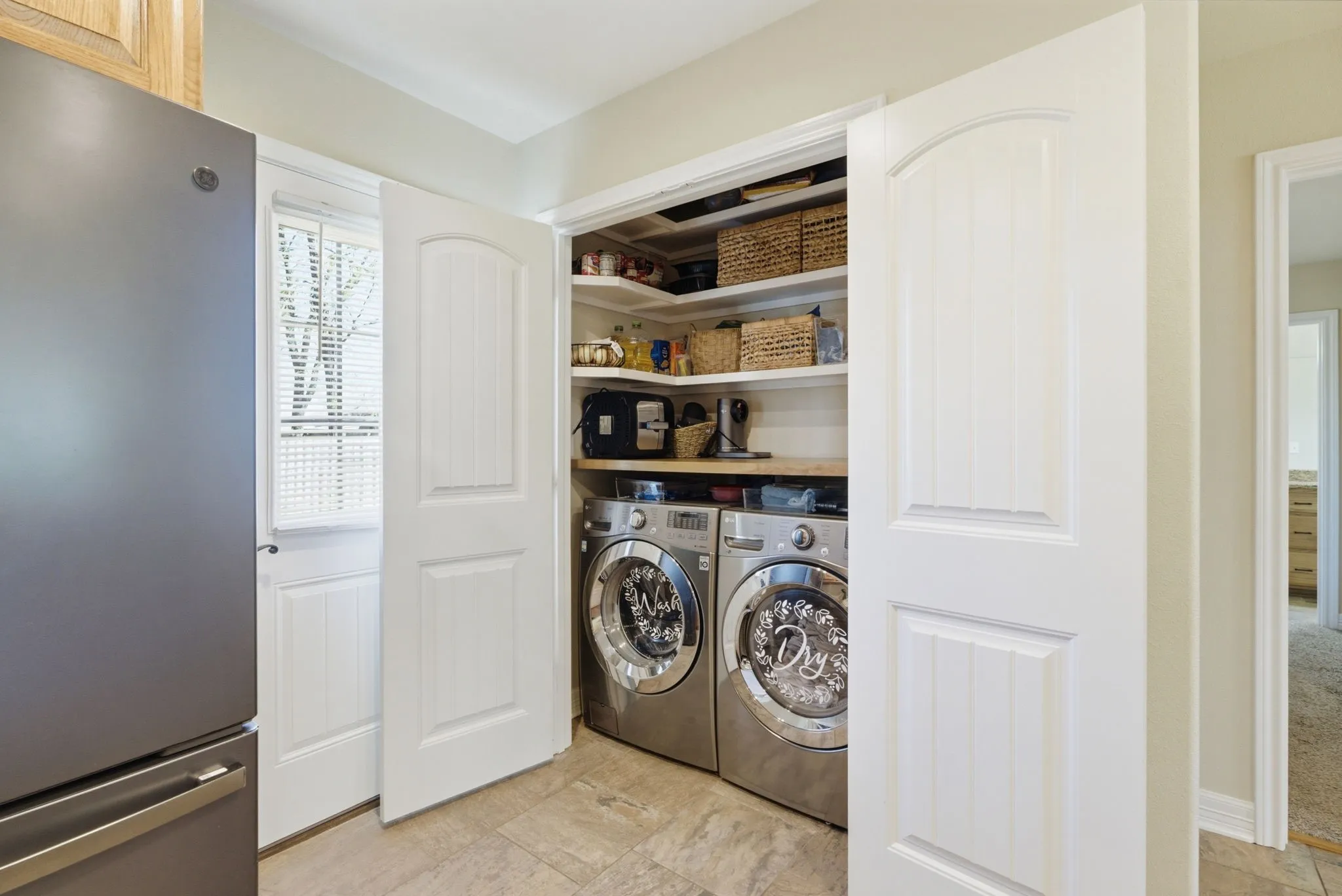 Built-in laundry appliances with wood-finish shelving, paneled doors, and tiled flooring