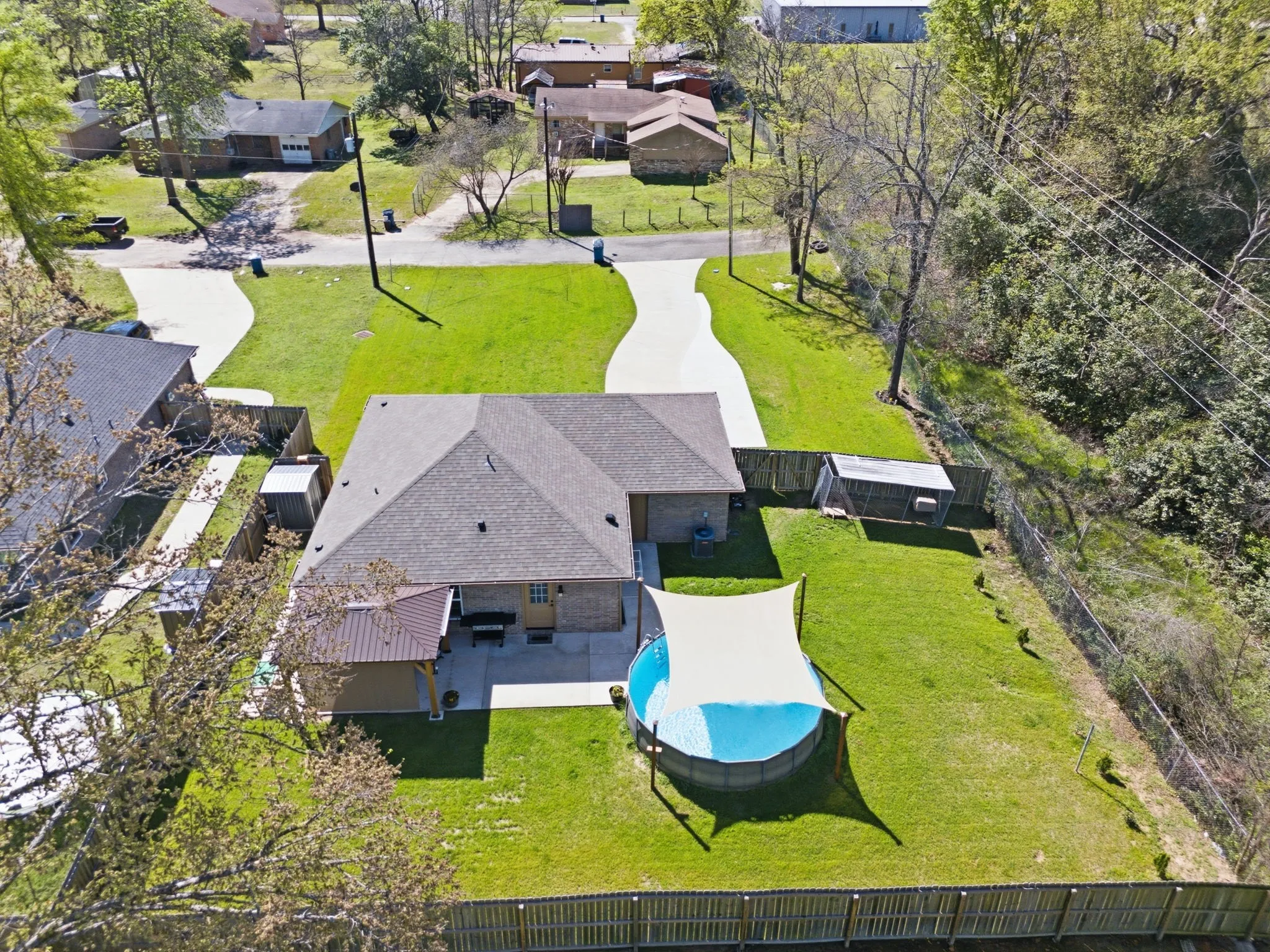 Expansive fenced yard with a pool, shade sail, and two storage sheds