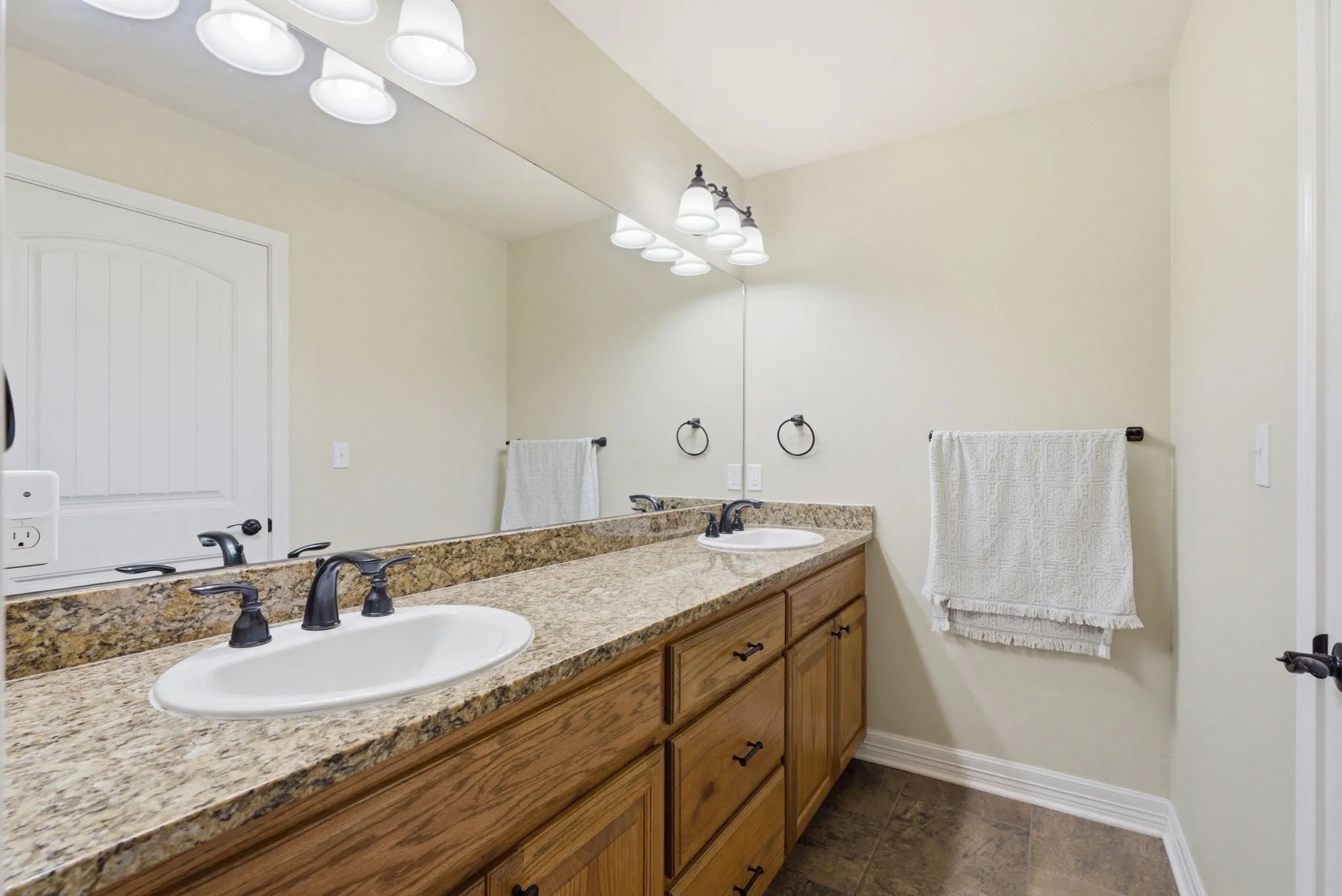 Dual vanity with a stone-finish countertop, wood-finish cabinetry, and oil-rubbed bronze fixtures