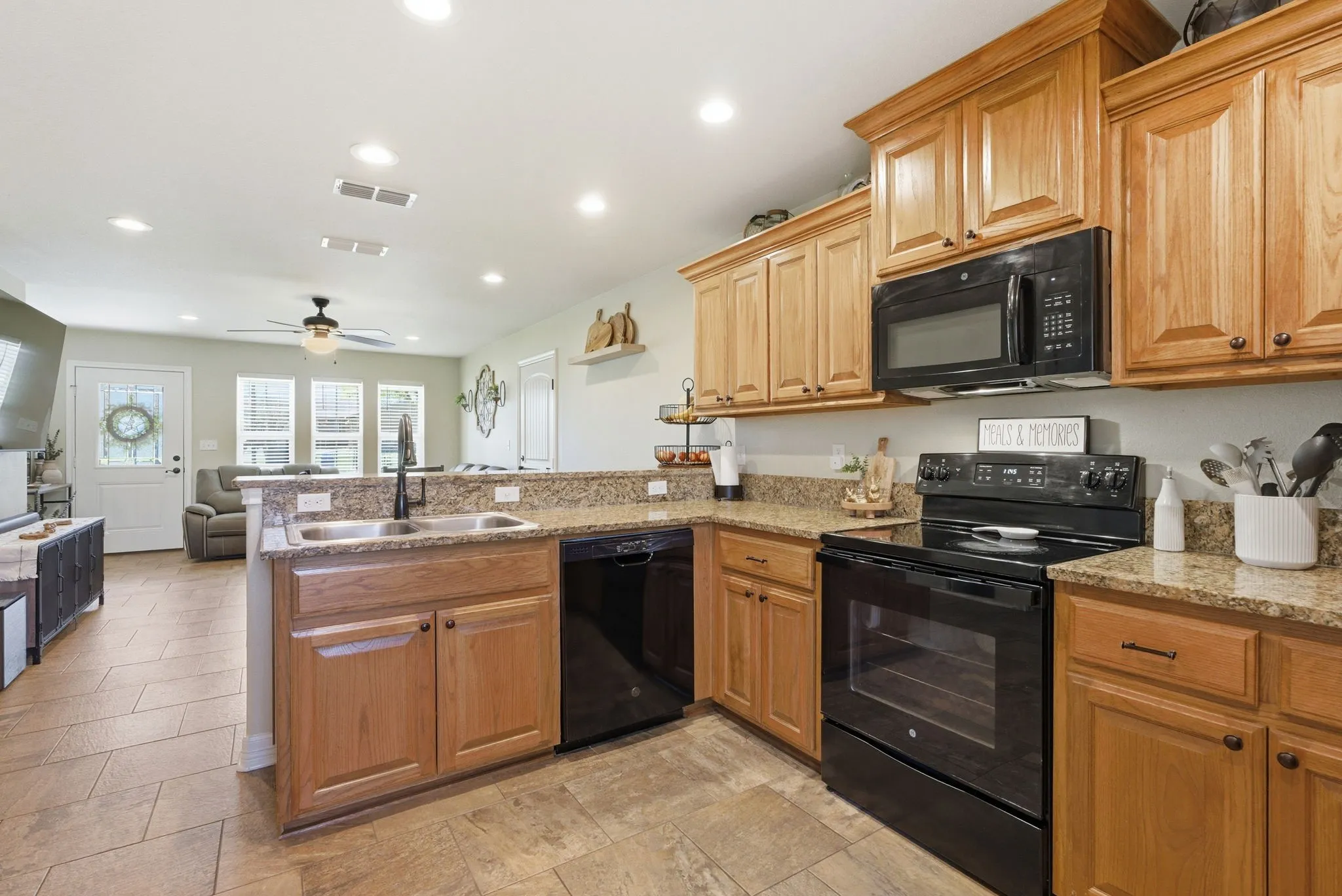 Kitchen featuring wood-finish cabinetry, granite countertops, an undermount double basin sink, and black appliances