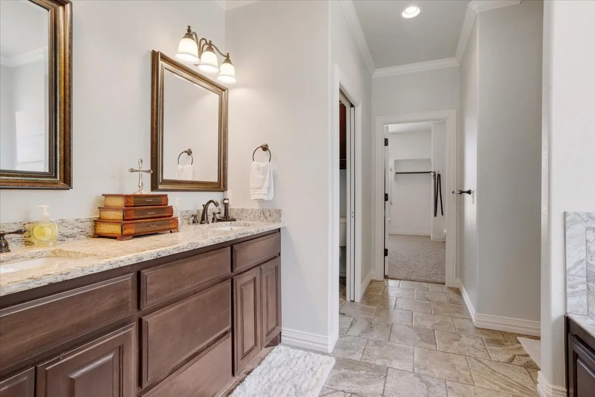 Dual sink vanity with granite countertop, wood-finish cabinetry, and framed mirrors