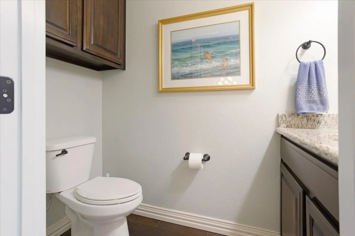 Wood-finish flooring, dark wood cabinetry, white toilet fixture, and a light-toned countertop