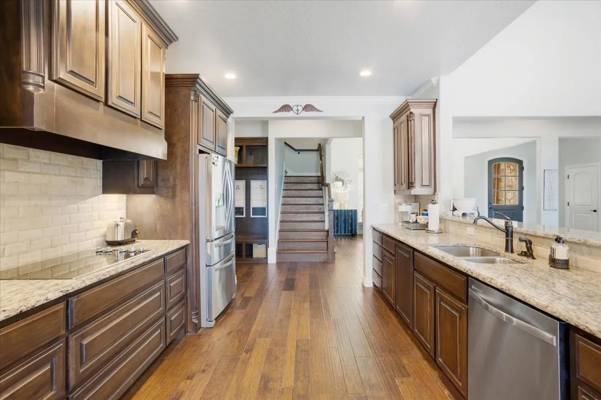 Kitchen featuring wood-finish flooring, dark wood cabinetry, light-toned countertops, a light brick-patterned backsplash, and stainless steel appliances