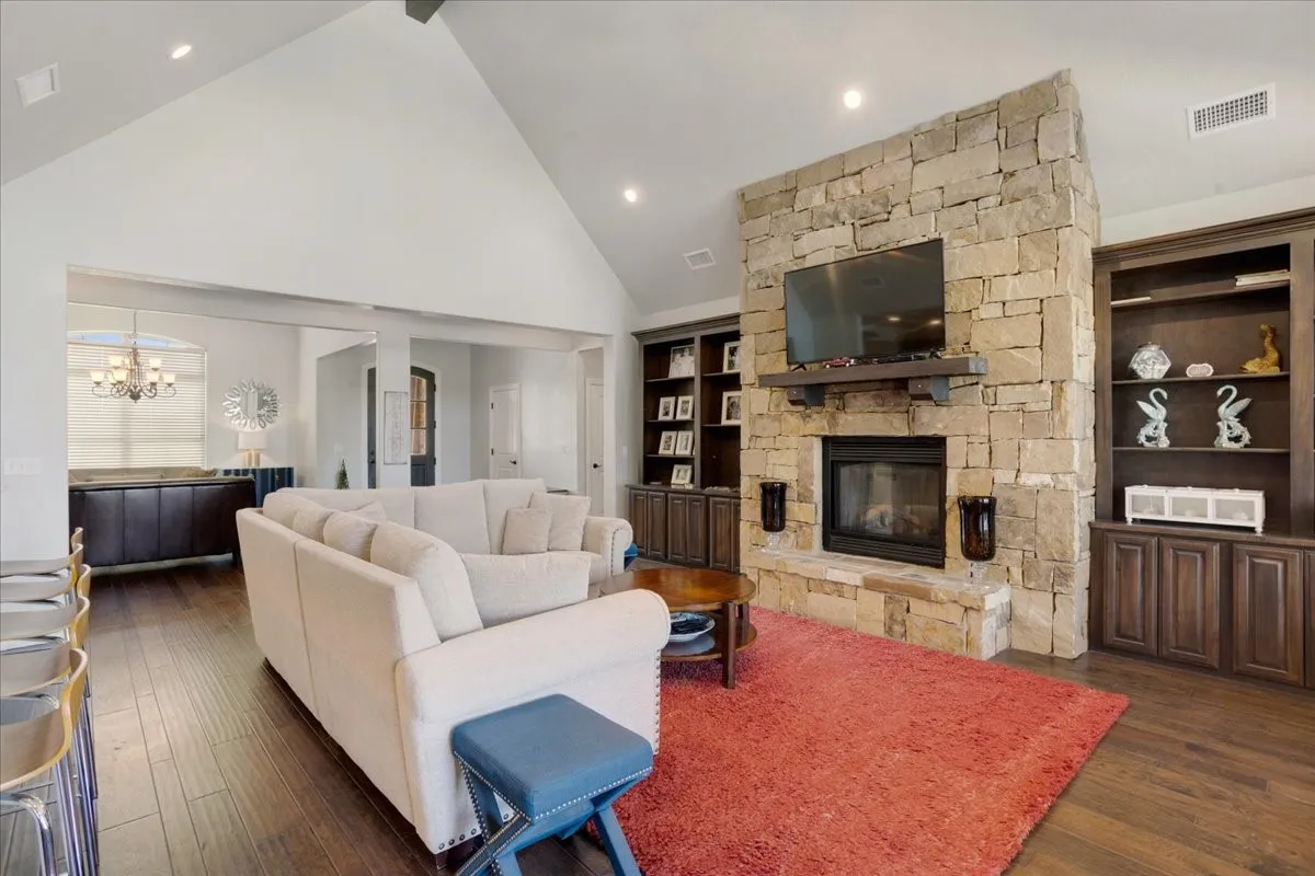 Stone-clad fireplace with a wood mantel, rich wood-finish flooring, recessed lighting, built-in cabinetry, and a vaulted ceiling