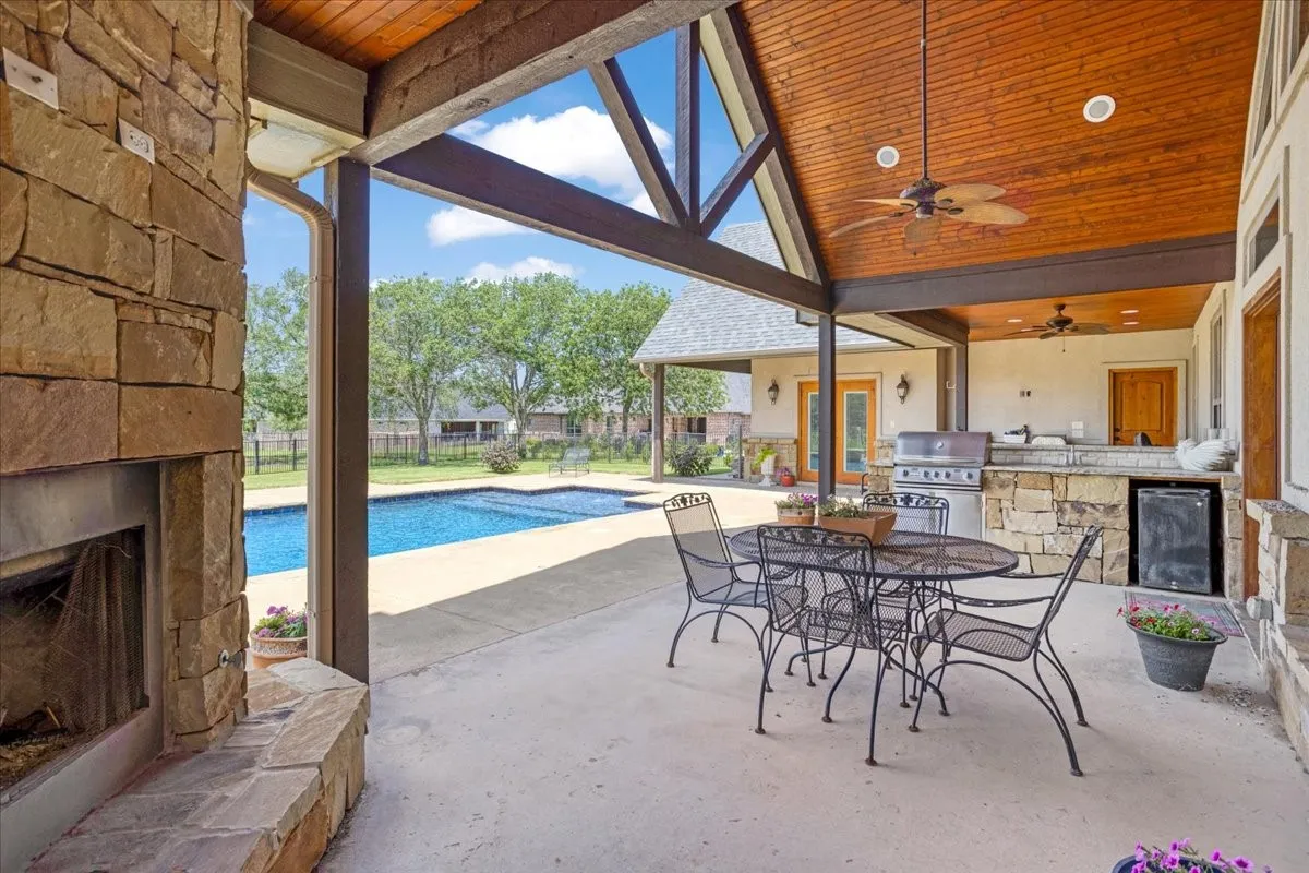 Covered patio with a stone-clad fireplace and an outdoor kitchen featuring a built-in grill