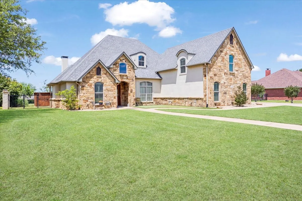 Stone and stucco exterior, arched window details, dormer windows, a prominent chimney, and a concrete pathway
