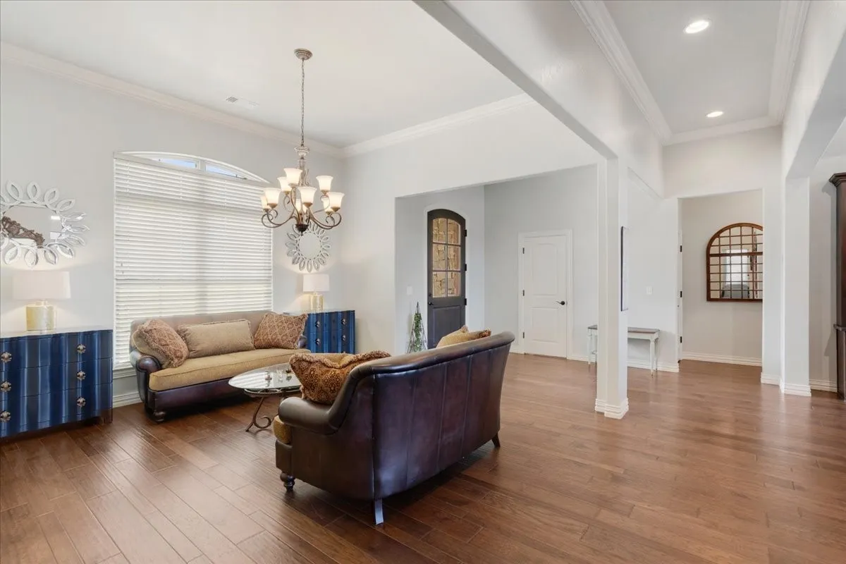 Wood-finish flooring throughout, tray ceiling with recessed lighting, arched window with horizontal blinds, iron chandelier, and white paneled interior doors