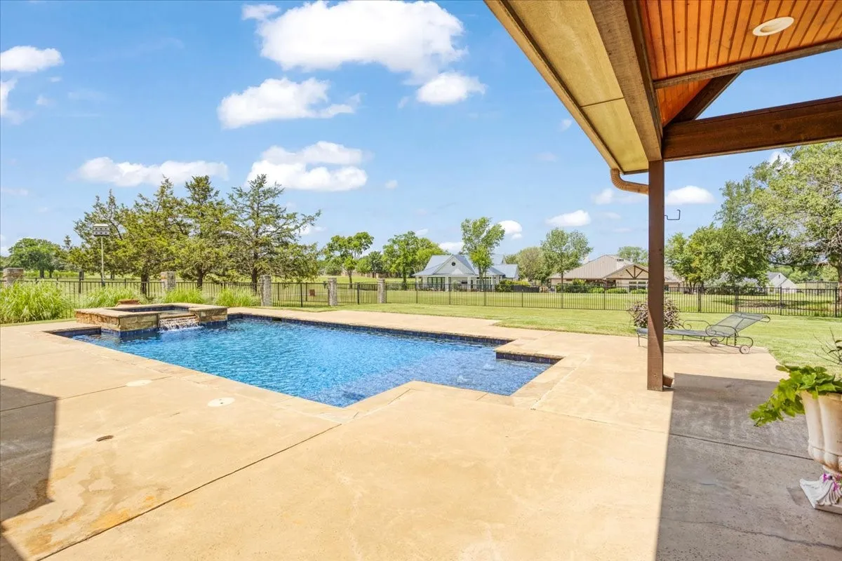 Swimming pool with integrated spa and stone surround, concrete decking, covered patio with wood-paneled ceiling, and expansive grassy yard