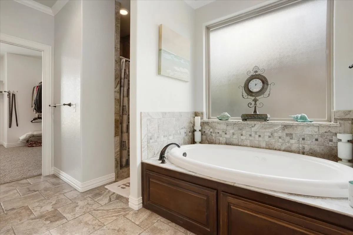 Soaking tub with mosaic tile surround, built-in dark wood cabinetry, and a privacy window